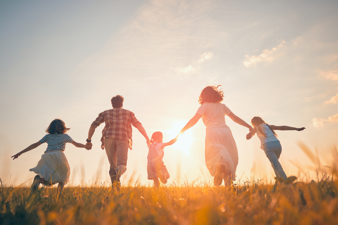 A family of 5 holding hands running together and there's a sunset ahead of them.