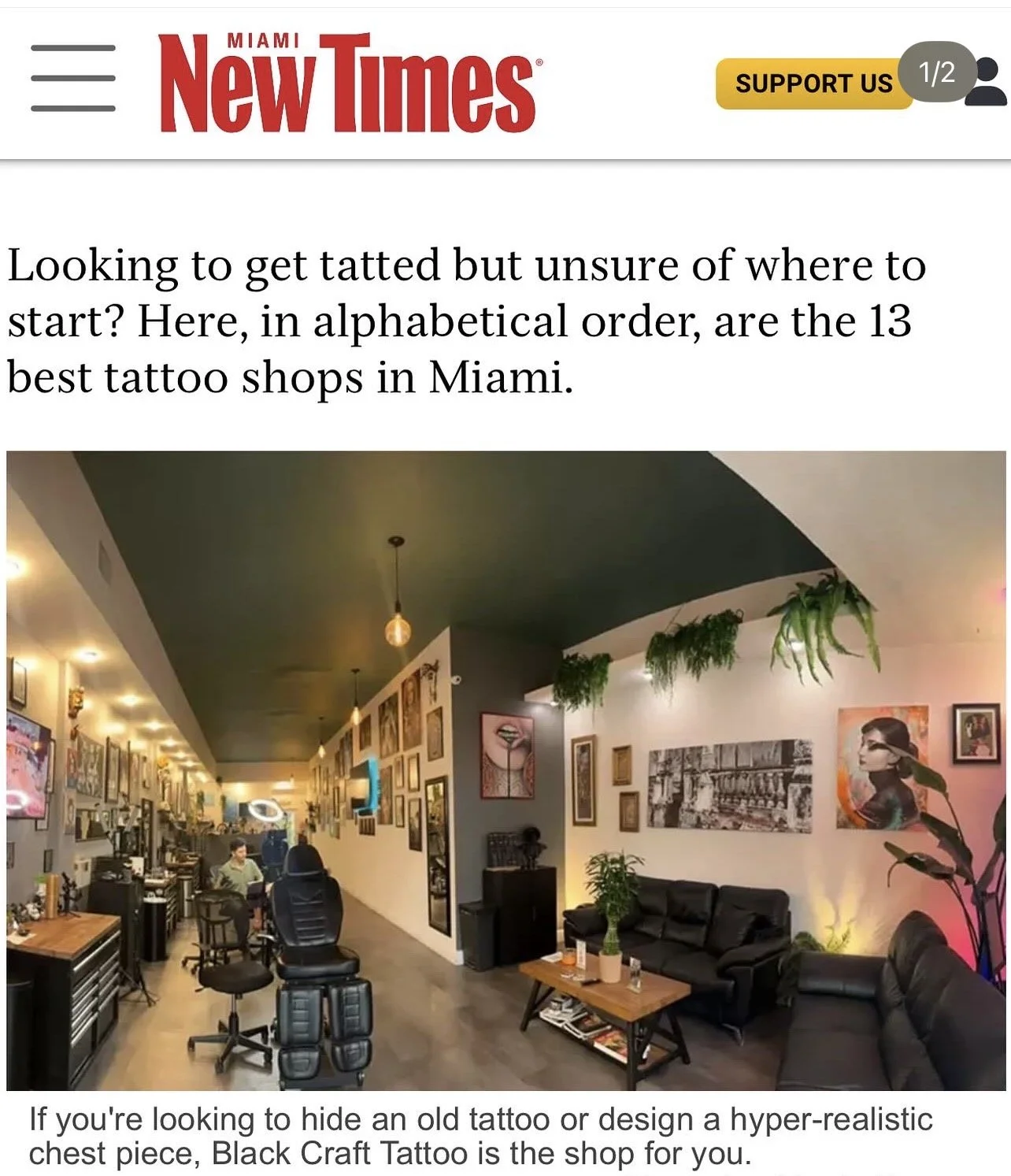 Interior of a tattoo shop with multiple framed art pieces on the walls, a black leather sofa, a coffee table, and tattoo artist chairs, with hanging plants and ambient lighting.