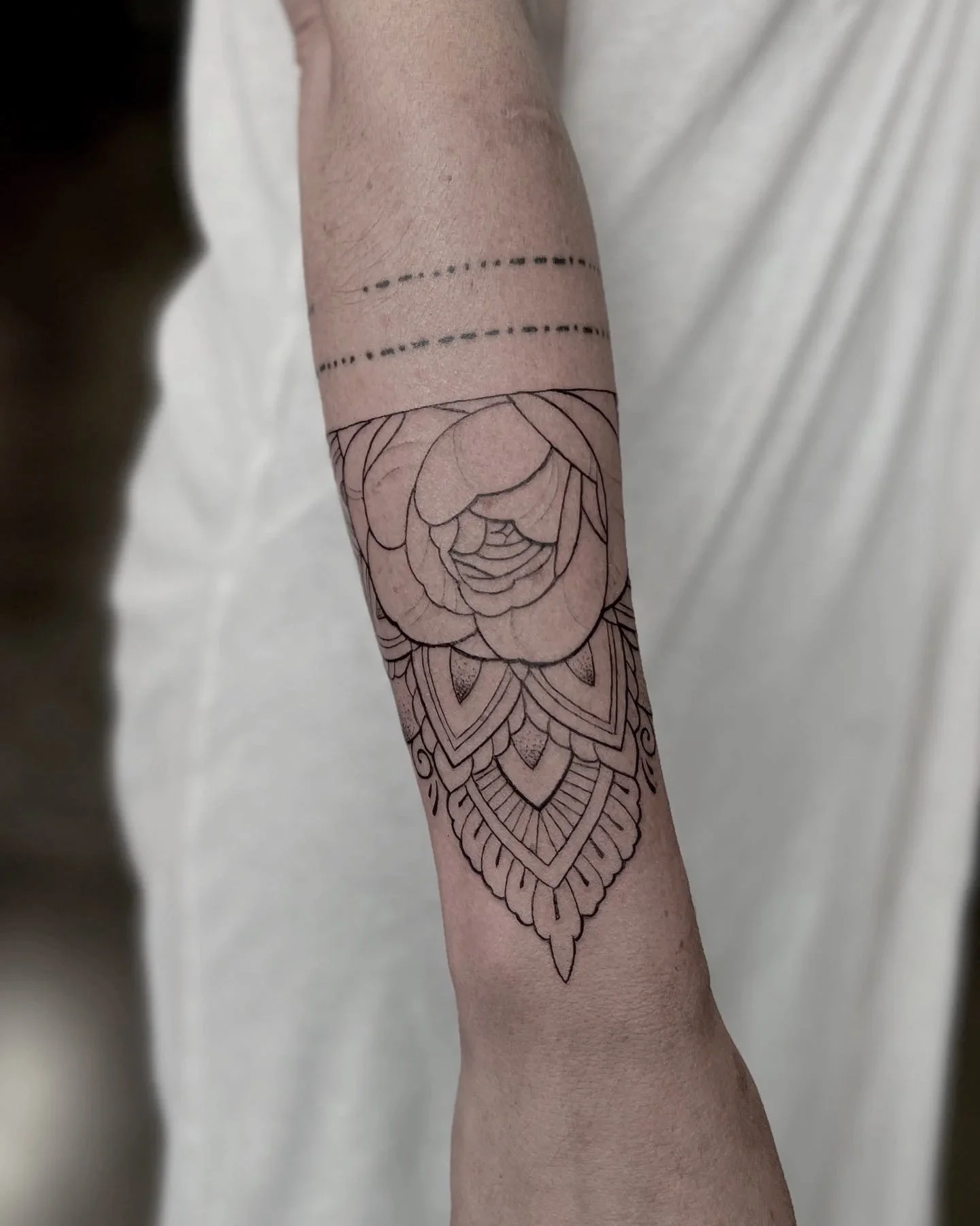 A person's forearm with a tattoo of a mandala and a large flower, with two dotted lines above the tattoo.