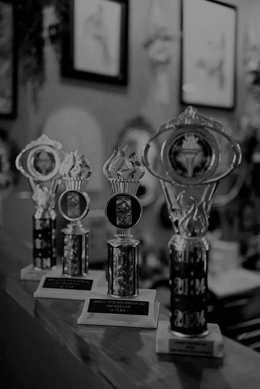 Trophies and awards on a wooden table at an art convention, with framed artwork on the wall in the background.