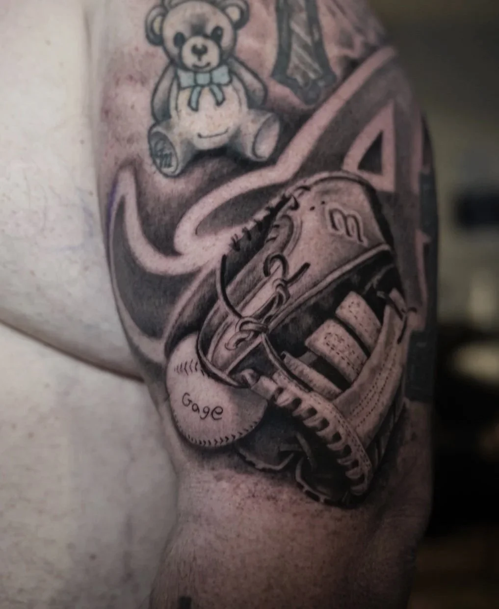 Tattoo of a baseball glove with a baseball labeled 'Gage', a pair of sneakers, and a teddy bear.