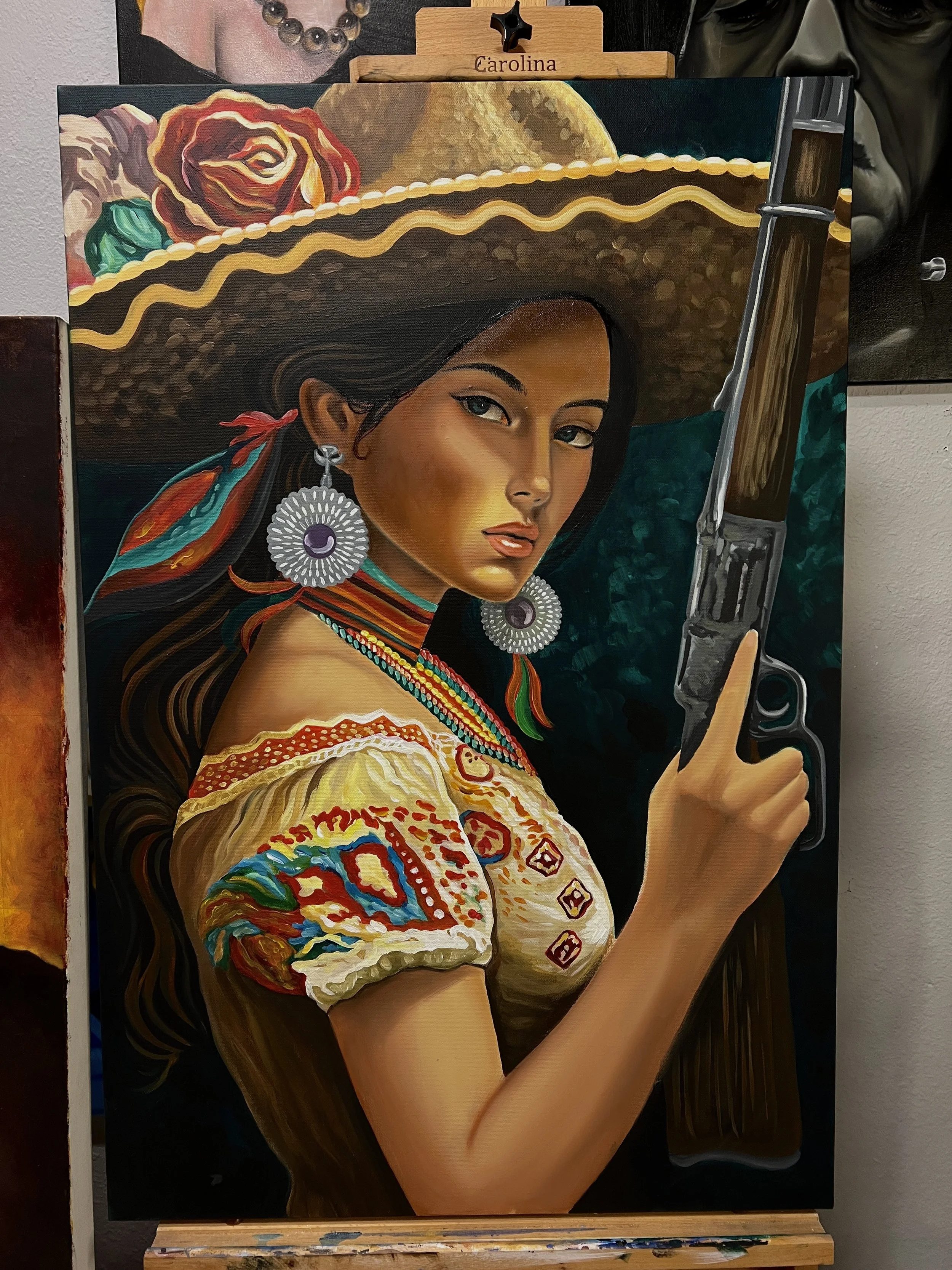 Painting of a woman with medium skin tone wearing a large straw hat decorated with a rose and a green leaf. She has long dark hair, large circular earrings, colorful necklaces, and a traditional embroidered dress with red, blue, and yellow designs. S