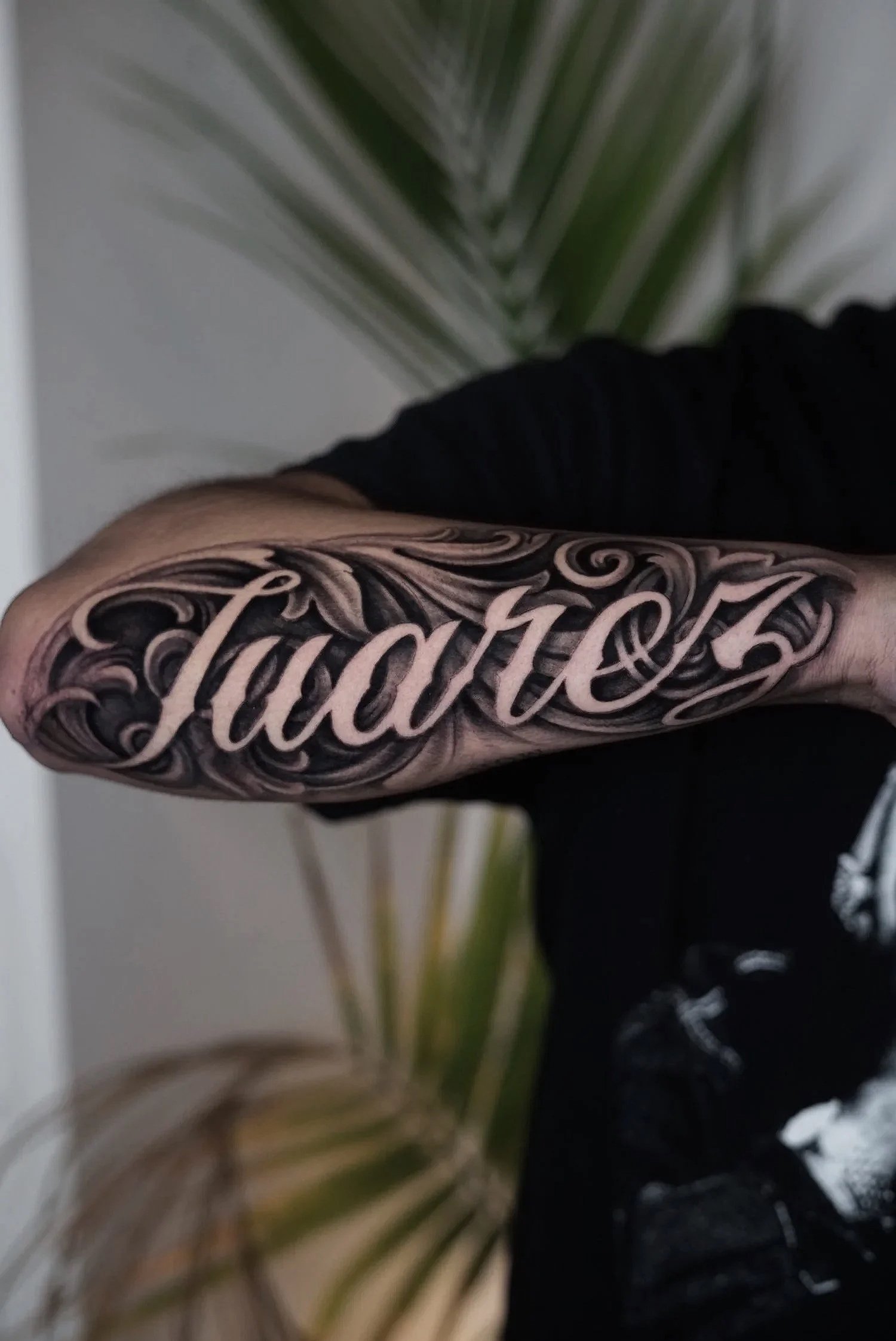 Close-up of a person's tattooed arm with the word 'Facto' in cursive, surrounded by intricate black and gray swirl designs.