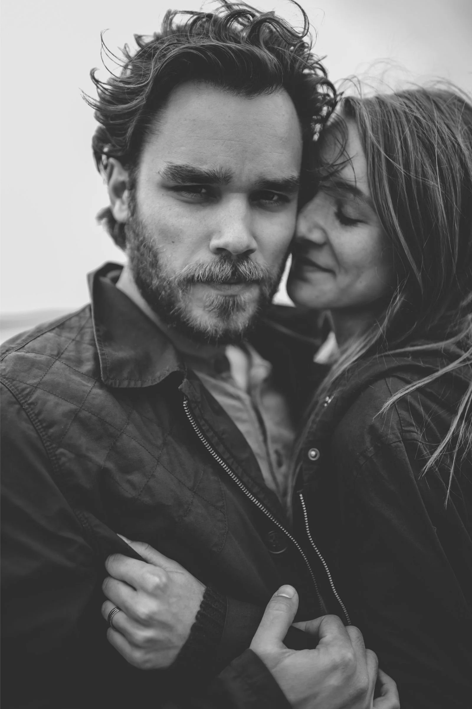 Black and white candid close-up of a man in a quilted jacket and a woman embracing affectionately, illustrating the impact of confidence on personal relationships.
