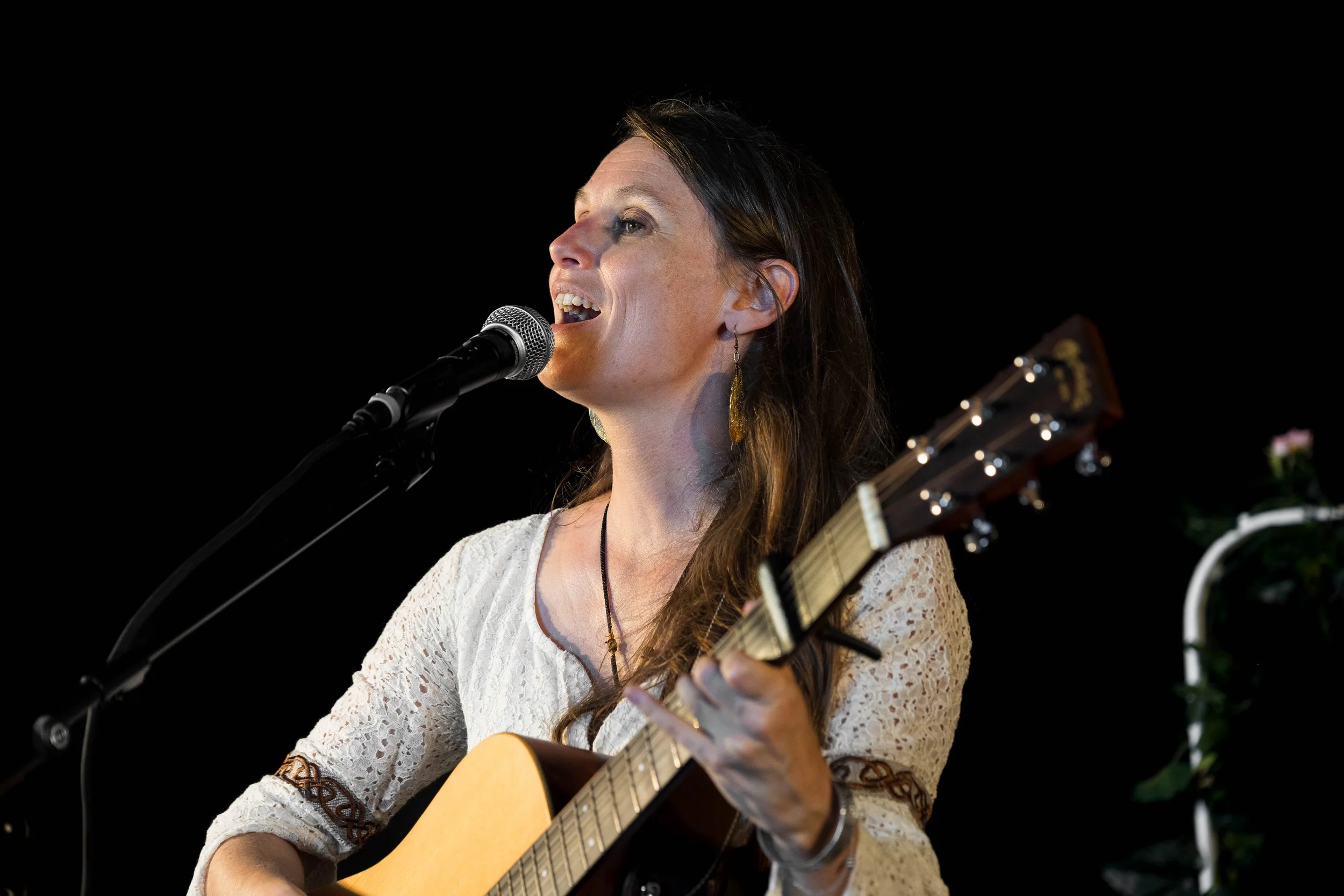 Une femme chante en jouant de la guitare, avec un micro devant elle, contre un fond noir.