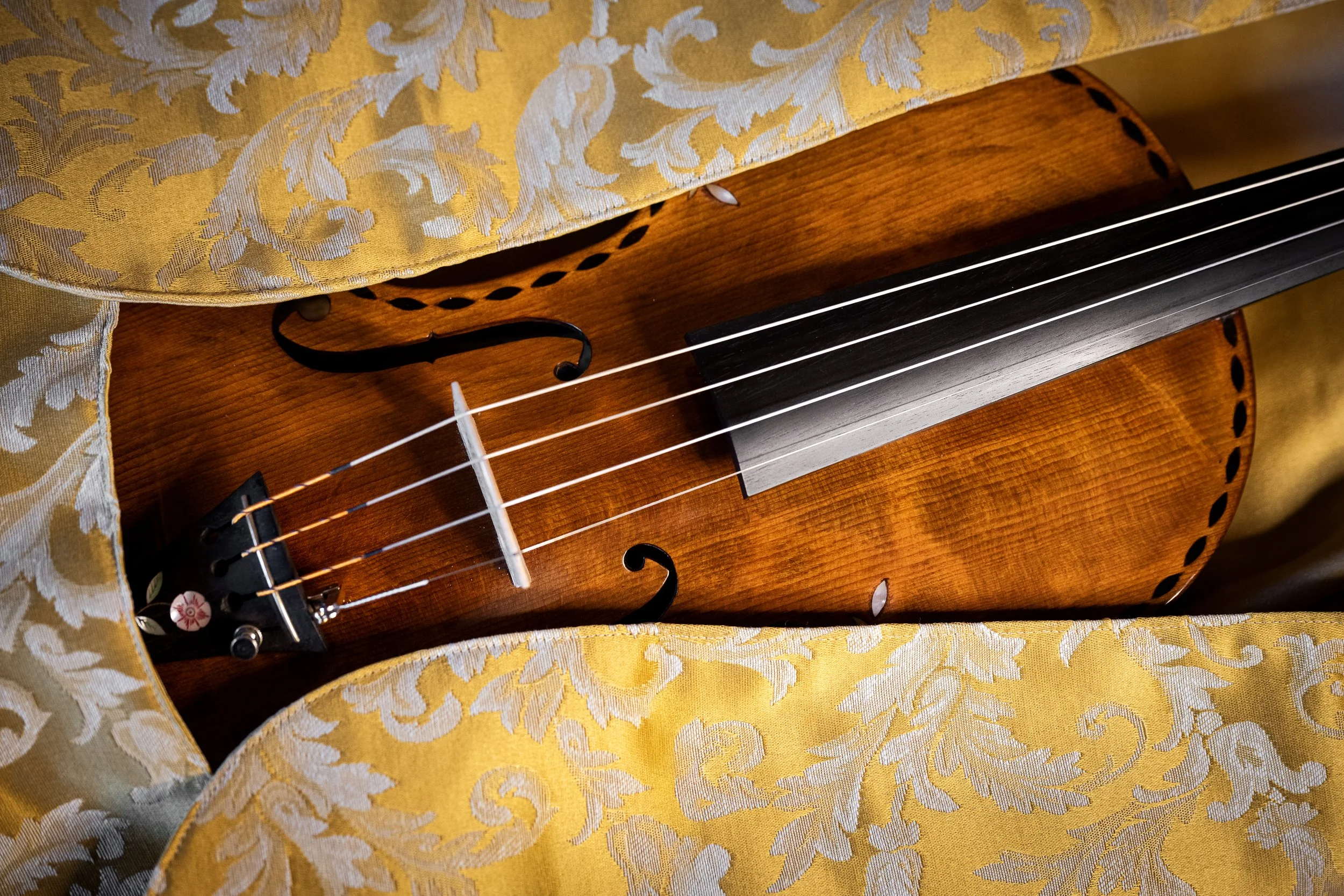 Guitare en bois posée sur un tissu orné de motifs dorés, avec des cordes et une rosace visible.