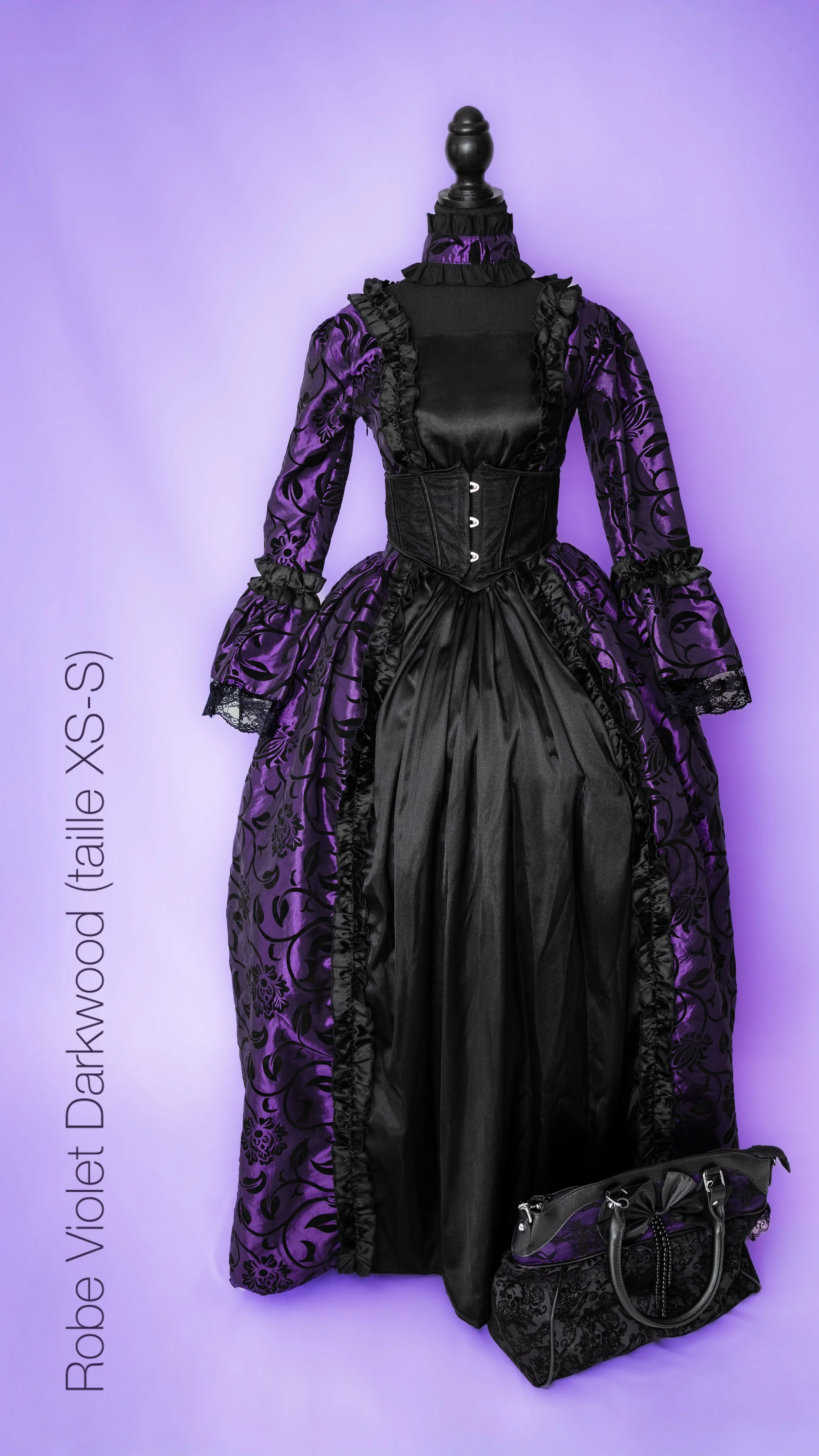 Une robe victorienne violette et noire avec un corset, une petite sacoche noire avec des détails violets, toutes exposées contre un fond violet
