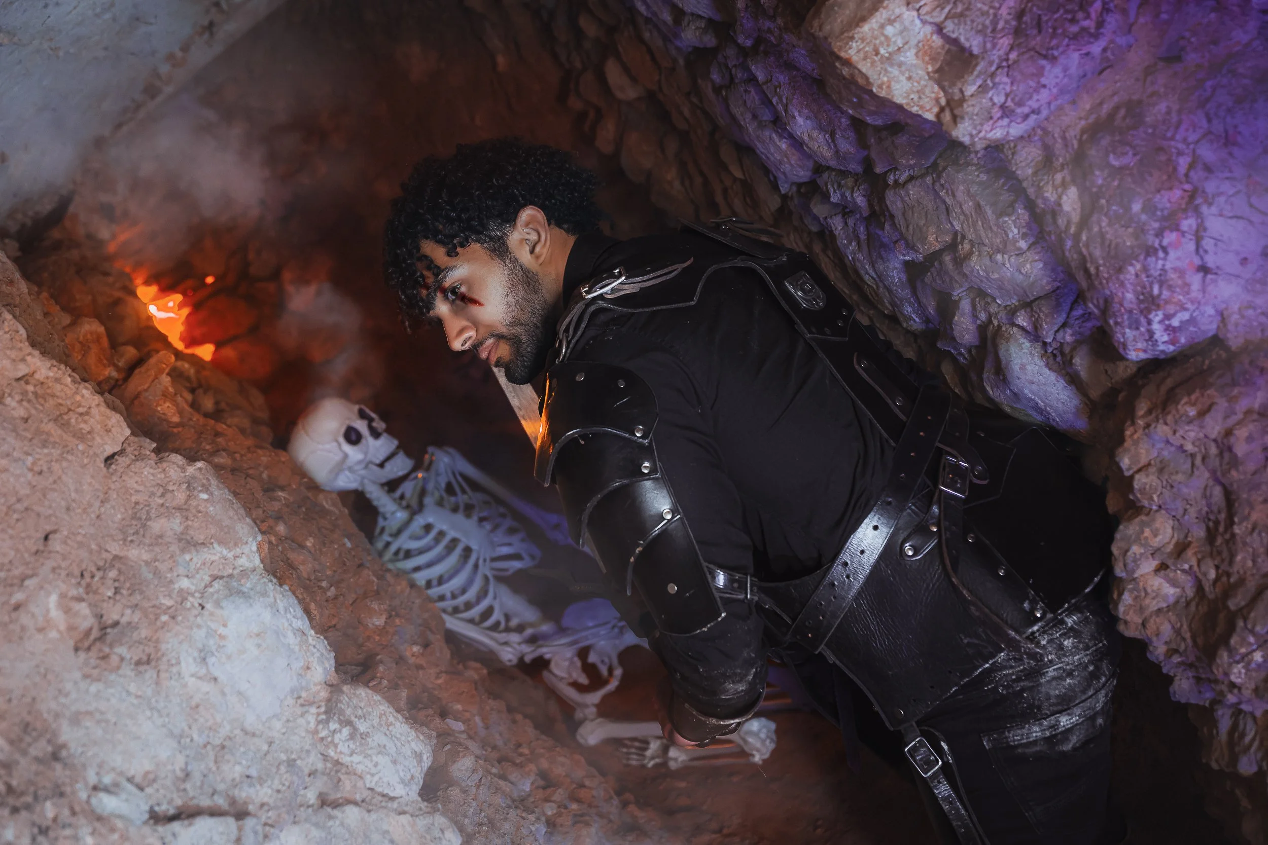 Homme déguisé en chevalier dans une grotte sombre avec squelettes et lumières colorées.