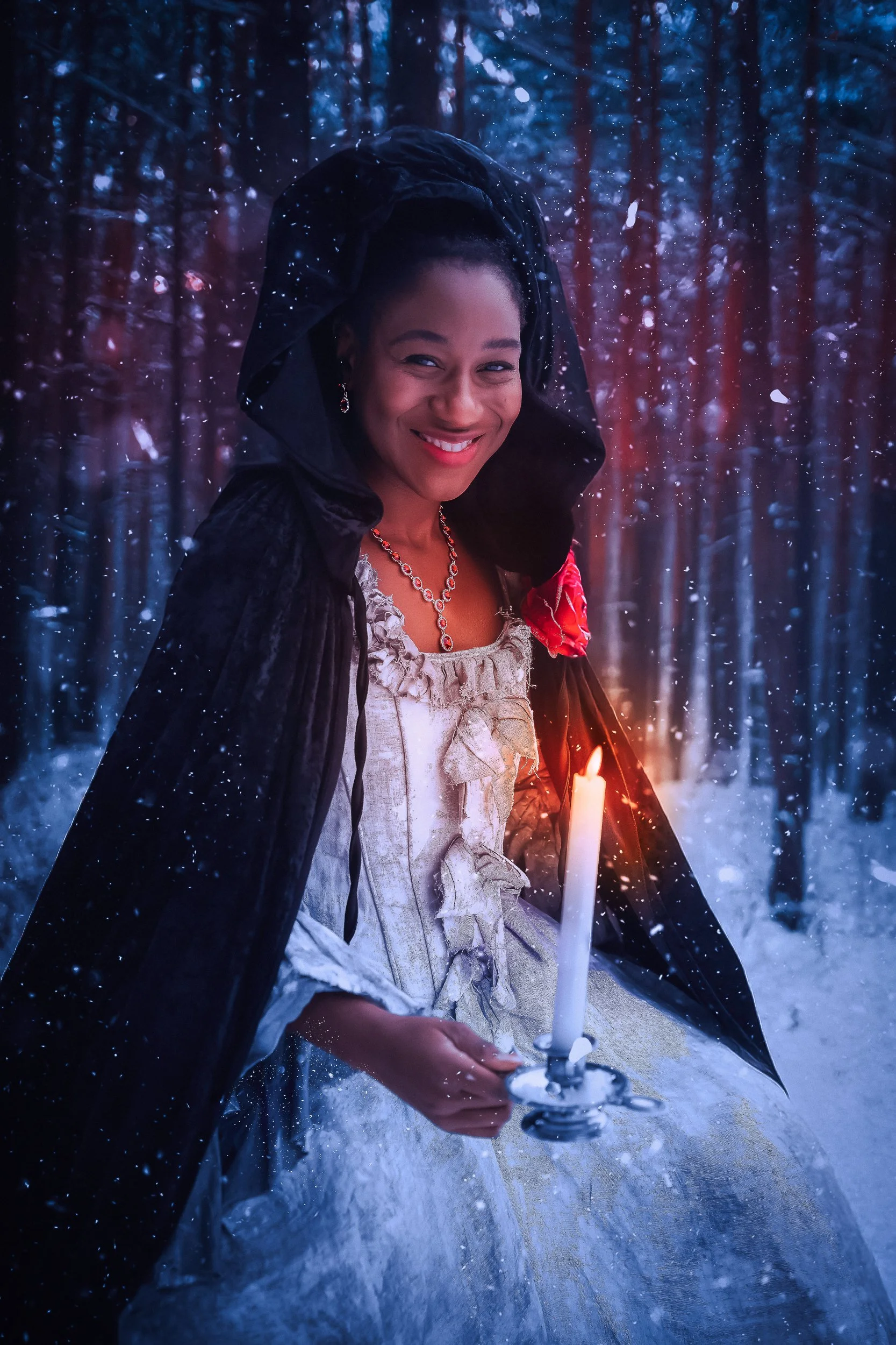 Femme souriante tenant une bougie dans une forêt enneigée pendant la nuit.