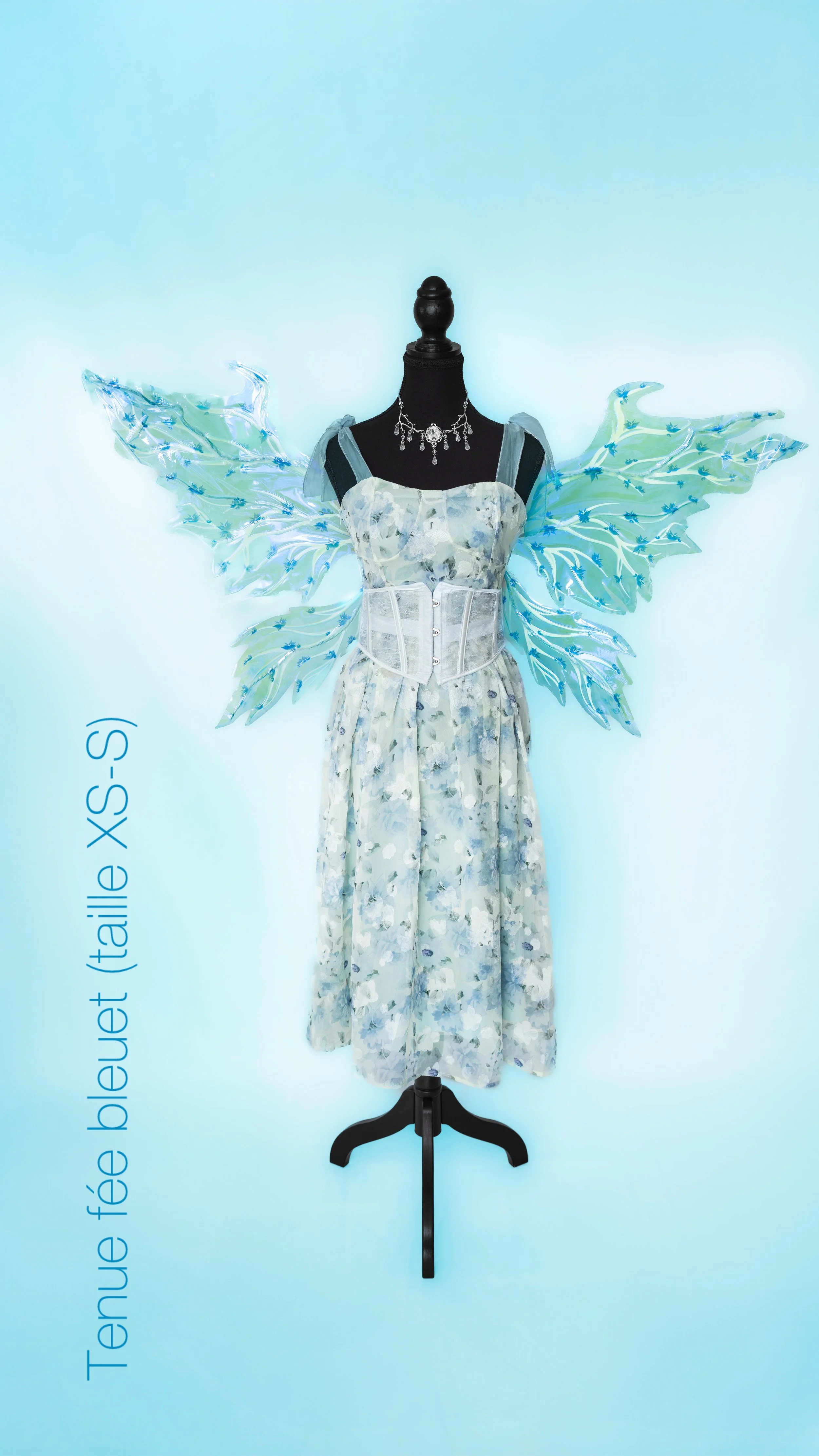 Vêtement de style robe avec des ailes de fée en plastique transparent et bleu attachées. Le mannequin porte également un collier élégant en perles et cristaux.