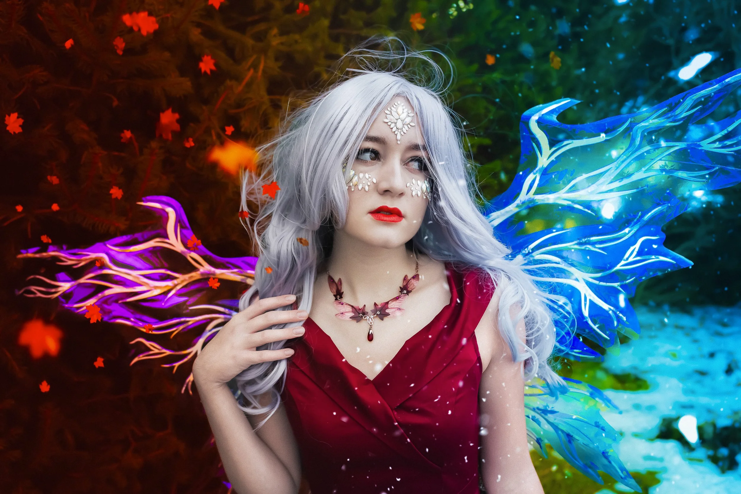Femme aux cheveux gris, maquillage décoratif floral, portant une robe rouge, avec des ailes lumineuses bleues et violettes, dans un décor coloré avec des feuilles lumineuses.