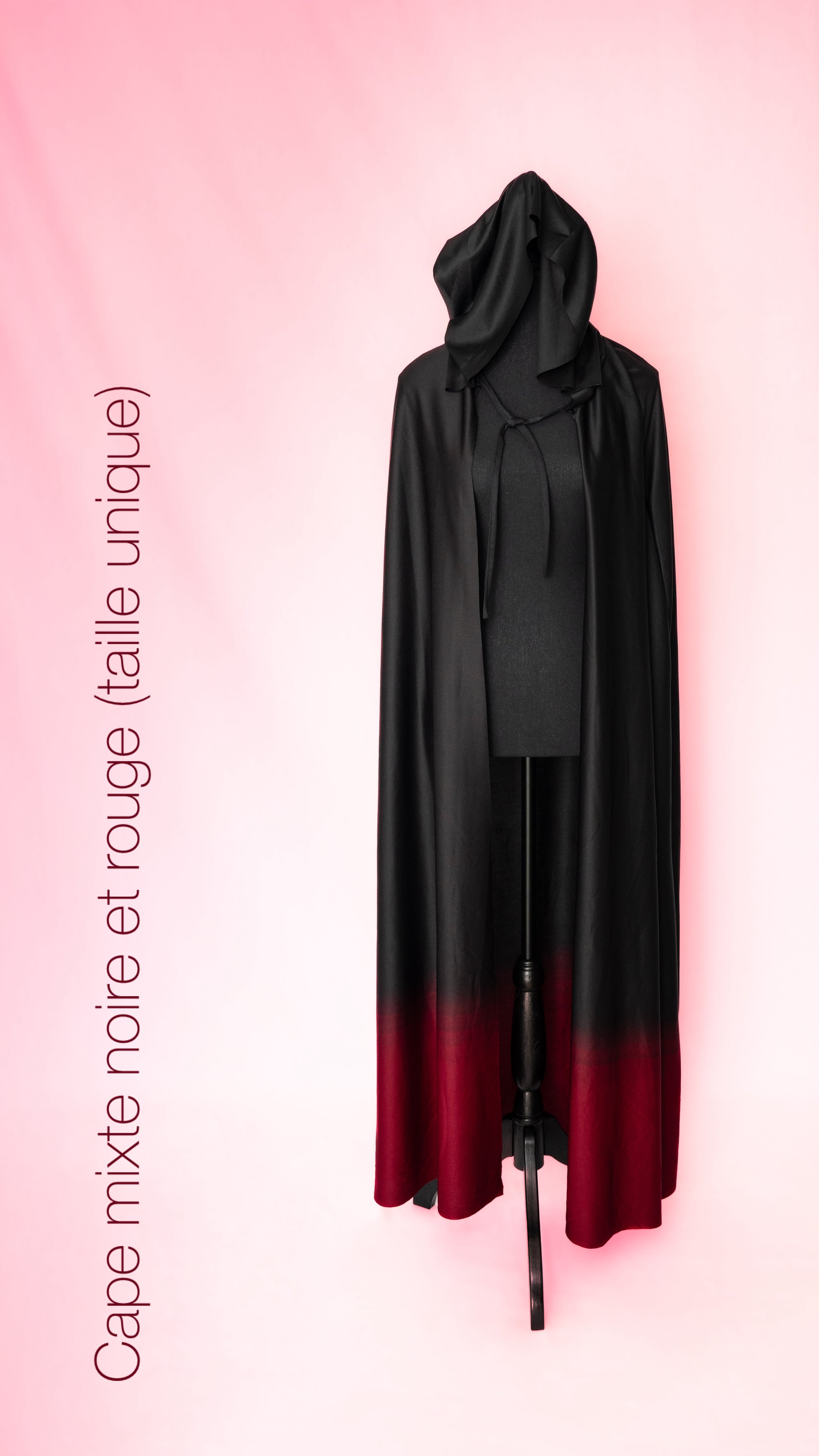 Un mannequin portant une cape noire avec une partie rouge en bas, exposée sur un fond rose pâle.