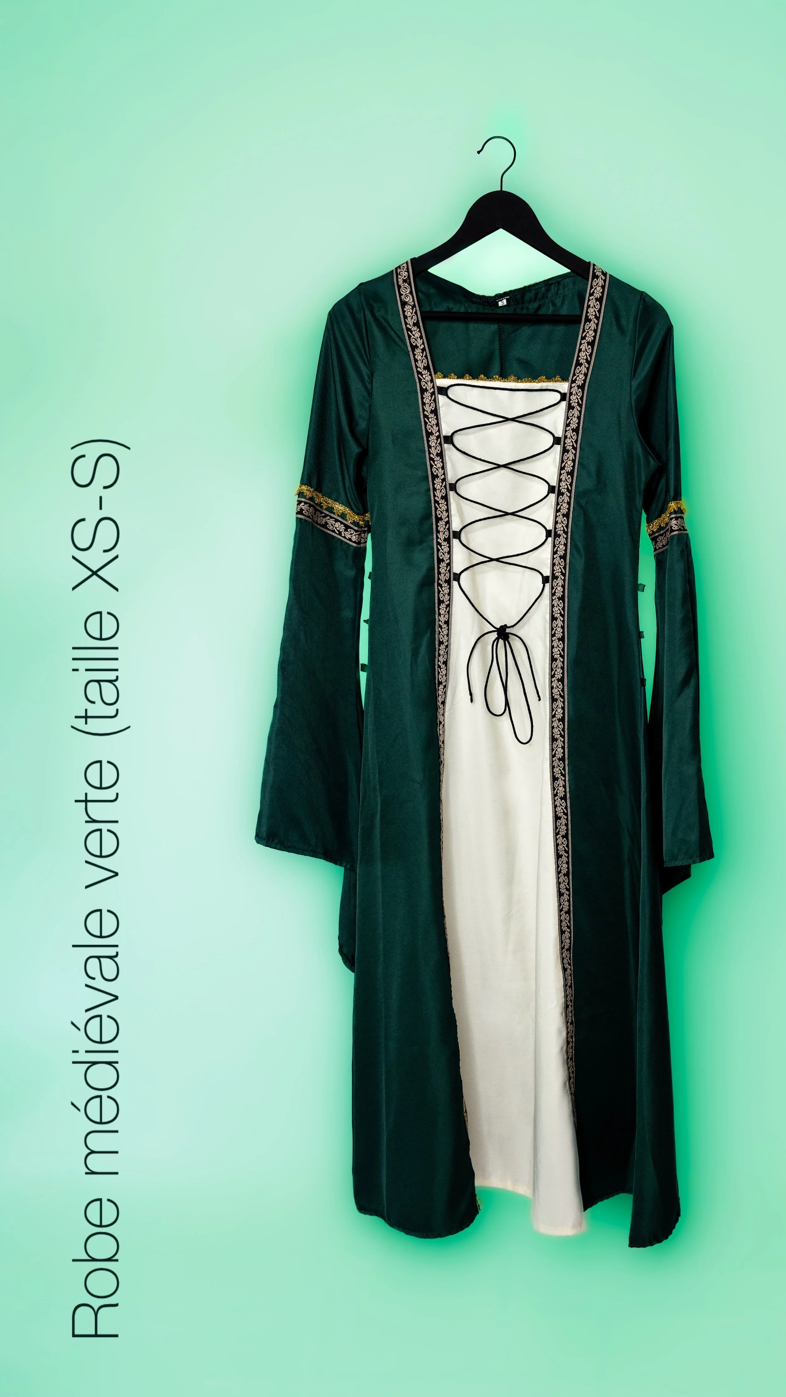 Robe médiévale verte avec manches longues et détails brodés, portant un corset blanc avec lacets noirs.