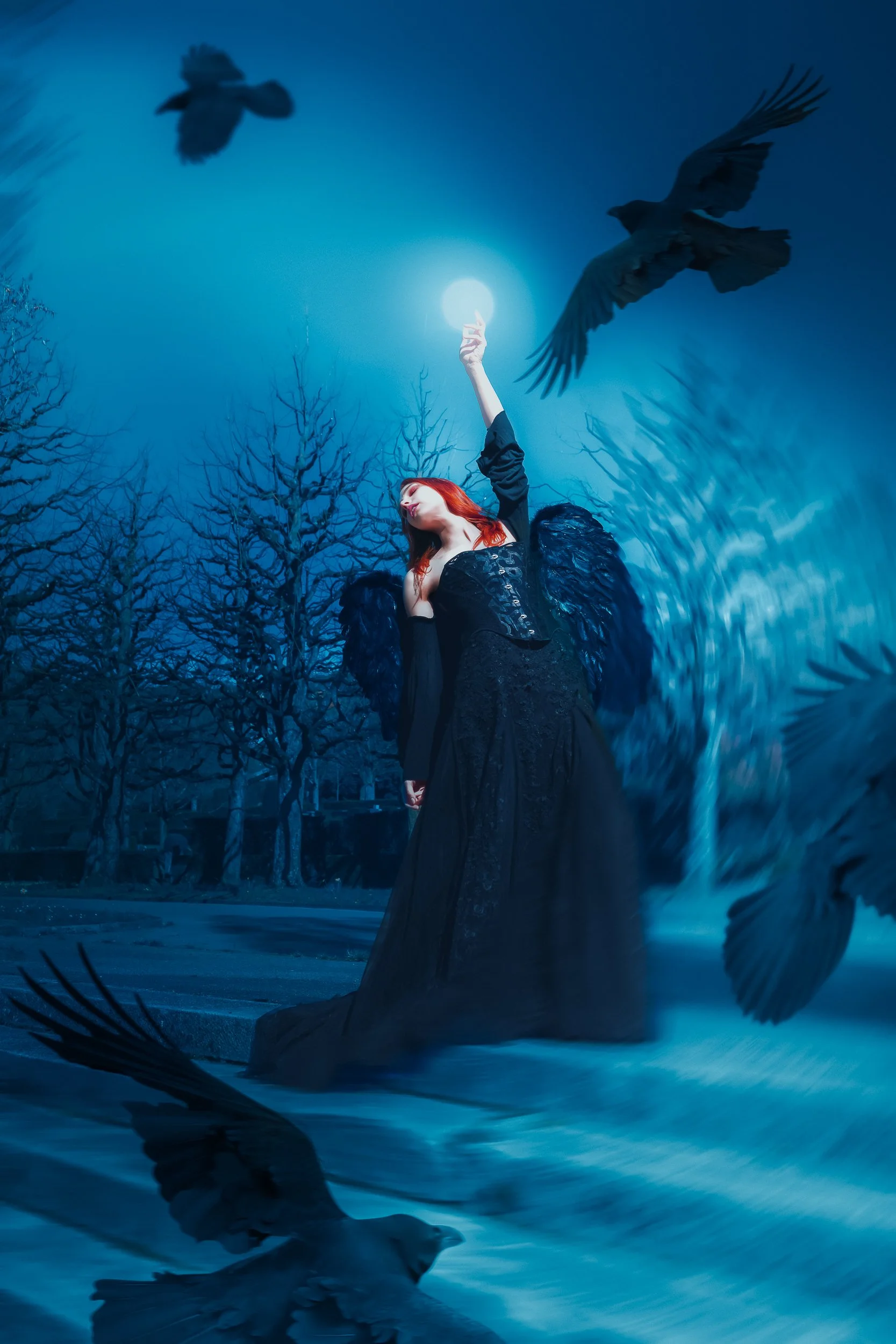 Une femme avec des ailes noires, portant une robe noire, se tient dans un paysage nocturne sous une pleine lune, entourée de plusieurs oiseaux en vol.