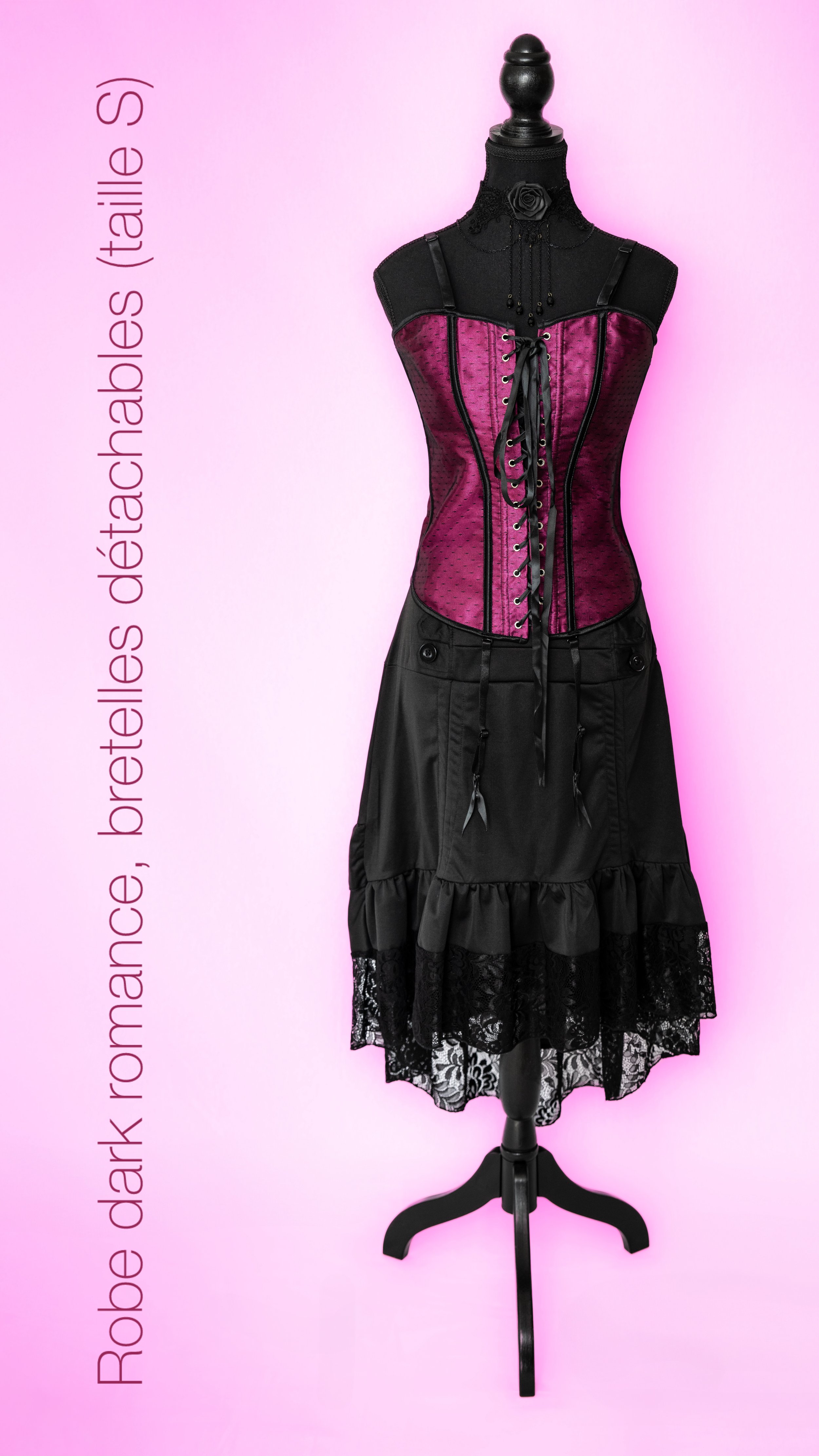 Un mannequin portant un corset violet avec des détails noirs, une jupe noire avec des volants en dentelle, contre un fond rose, avec du texte indiquant des tailles de robes, de bustes et de tailles en italien.
