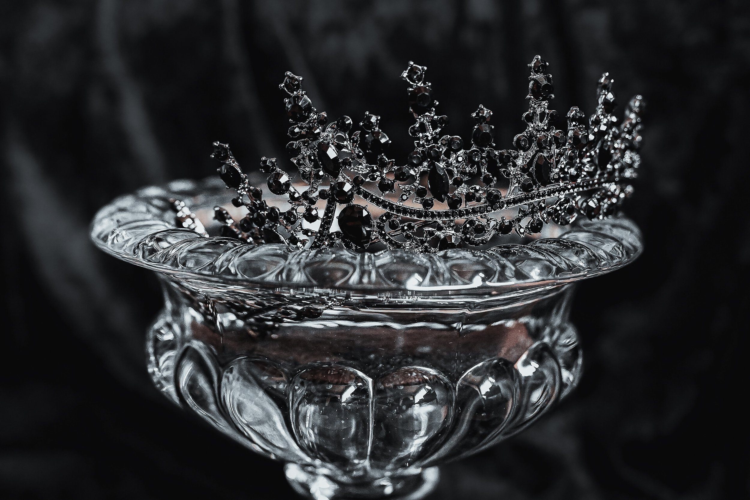 Une couronne de bijoux noirs posée dans un bol en verre clair avec un fond sombre.