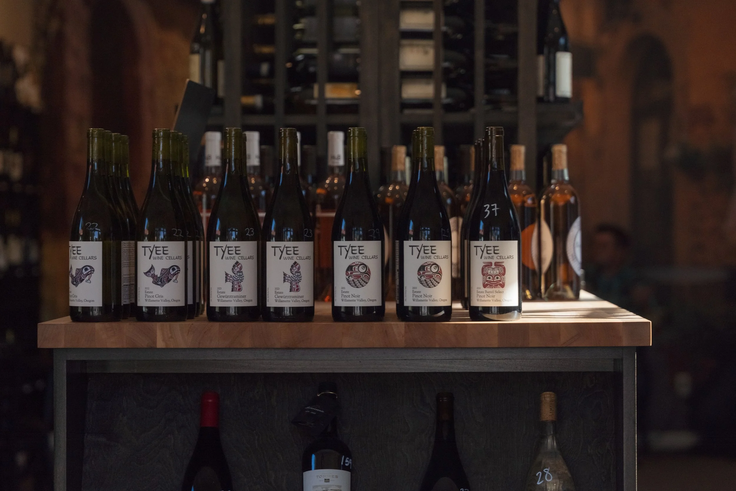 Bottles of wine displayed on a wooden shelf at a wine store or winery, with labels showing various types of wine from Willamette Valley, Oregon.