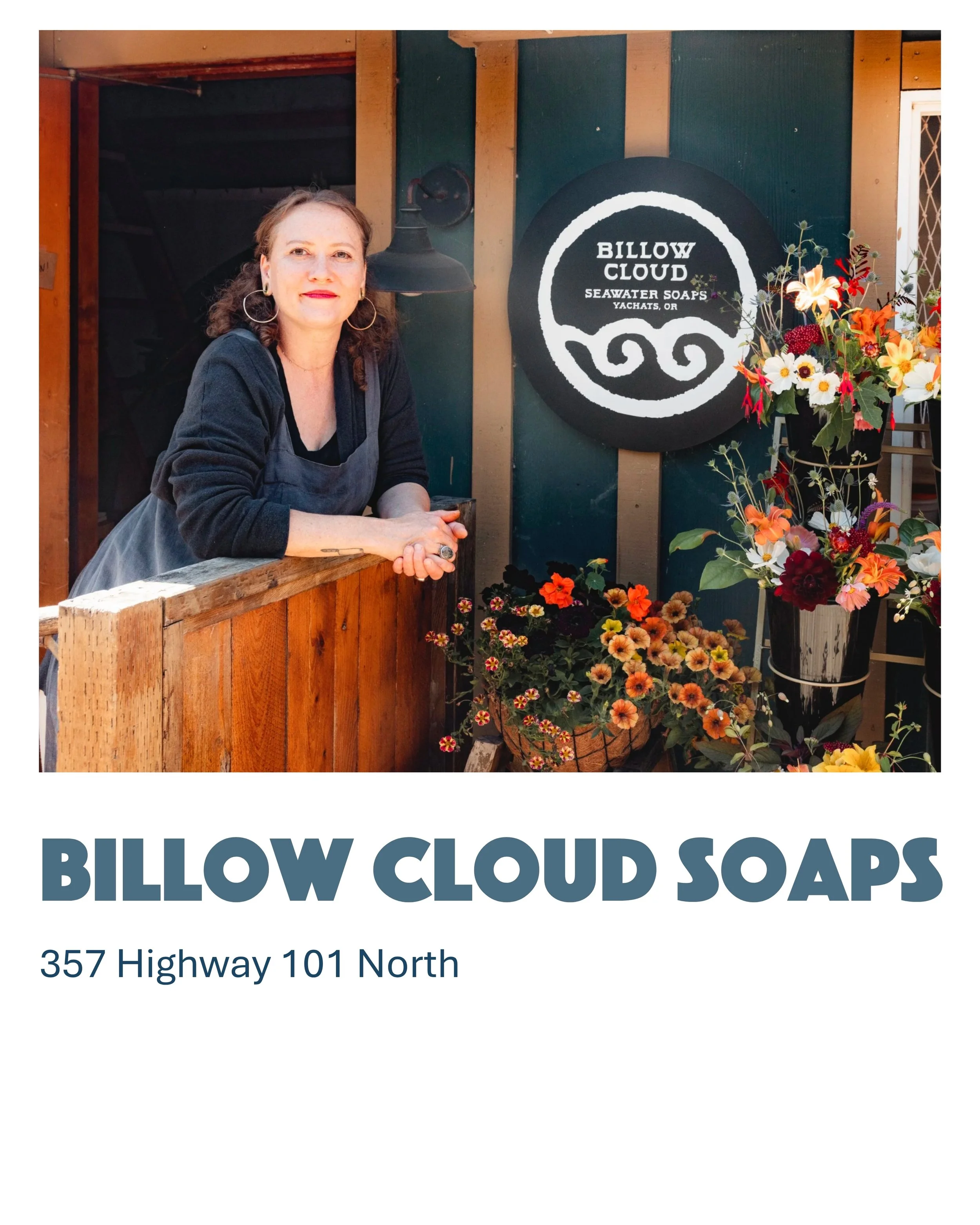 A woman in a black shirt and apron leaning on a wooden railing in front of a sign that reads "Billow Cloud Seawater Soaps," with colorful flowers on display nearby.