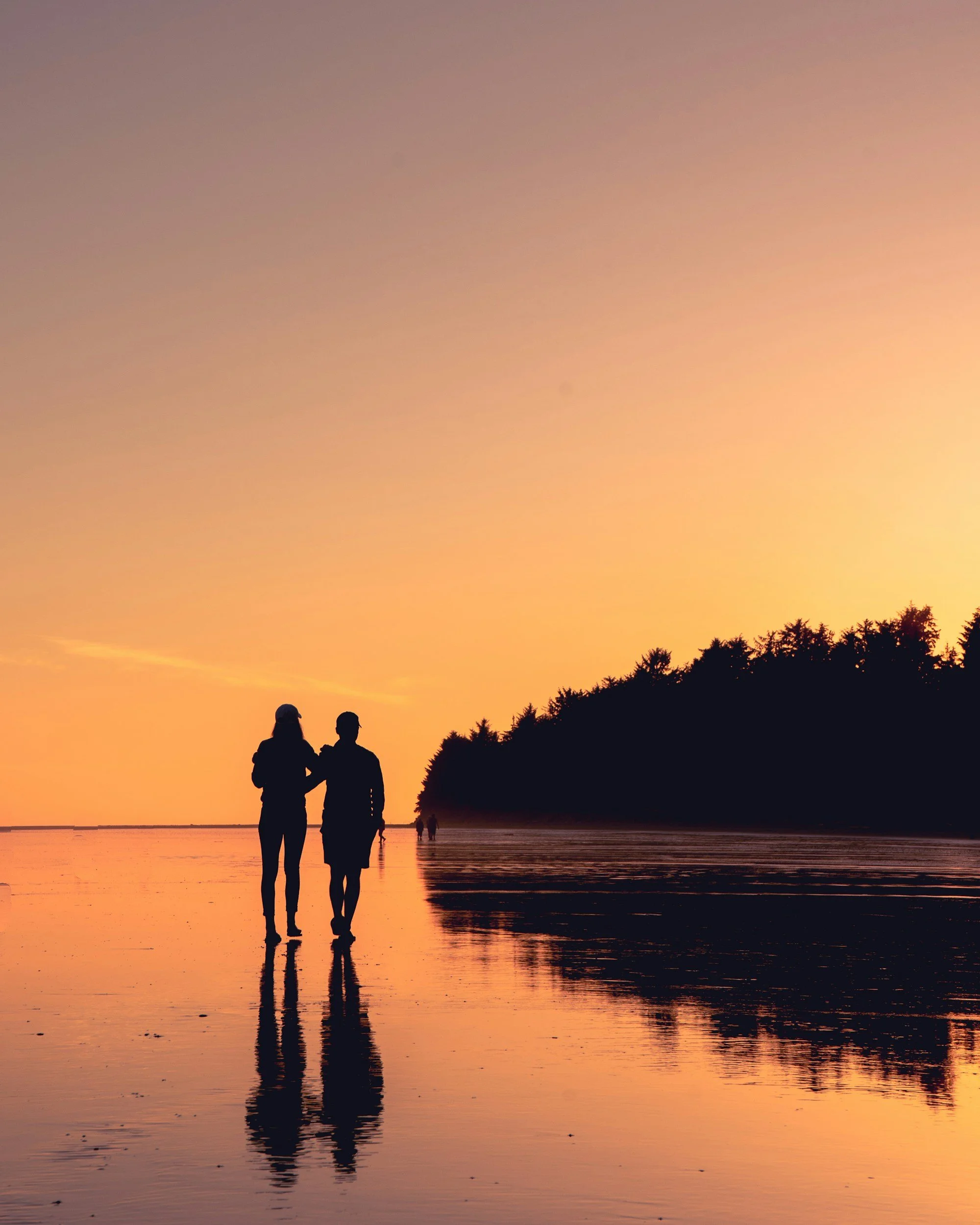 Silhouettes of a couple walking on the beach at sunset with a sunset sky and reflection in the water.