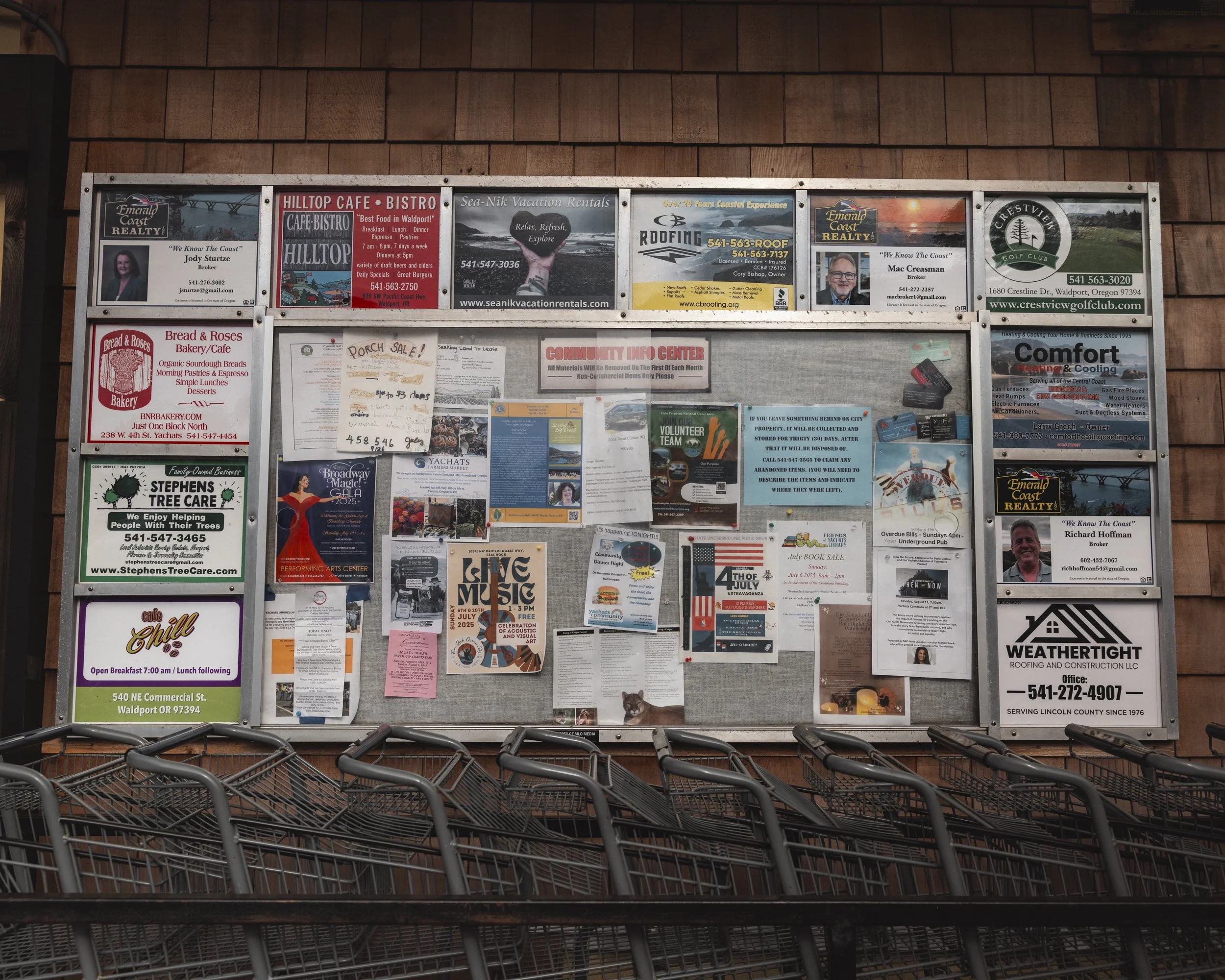 Community bulletin board with flyers and advertisements in a shopping area, surrounded by shopping carts.