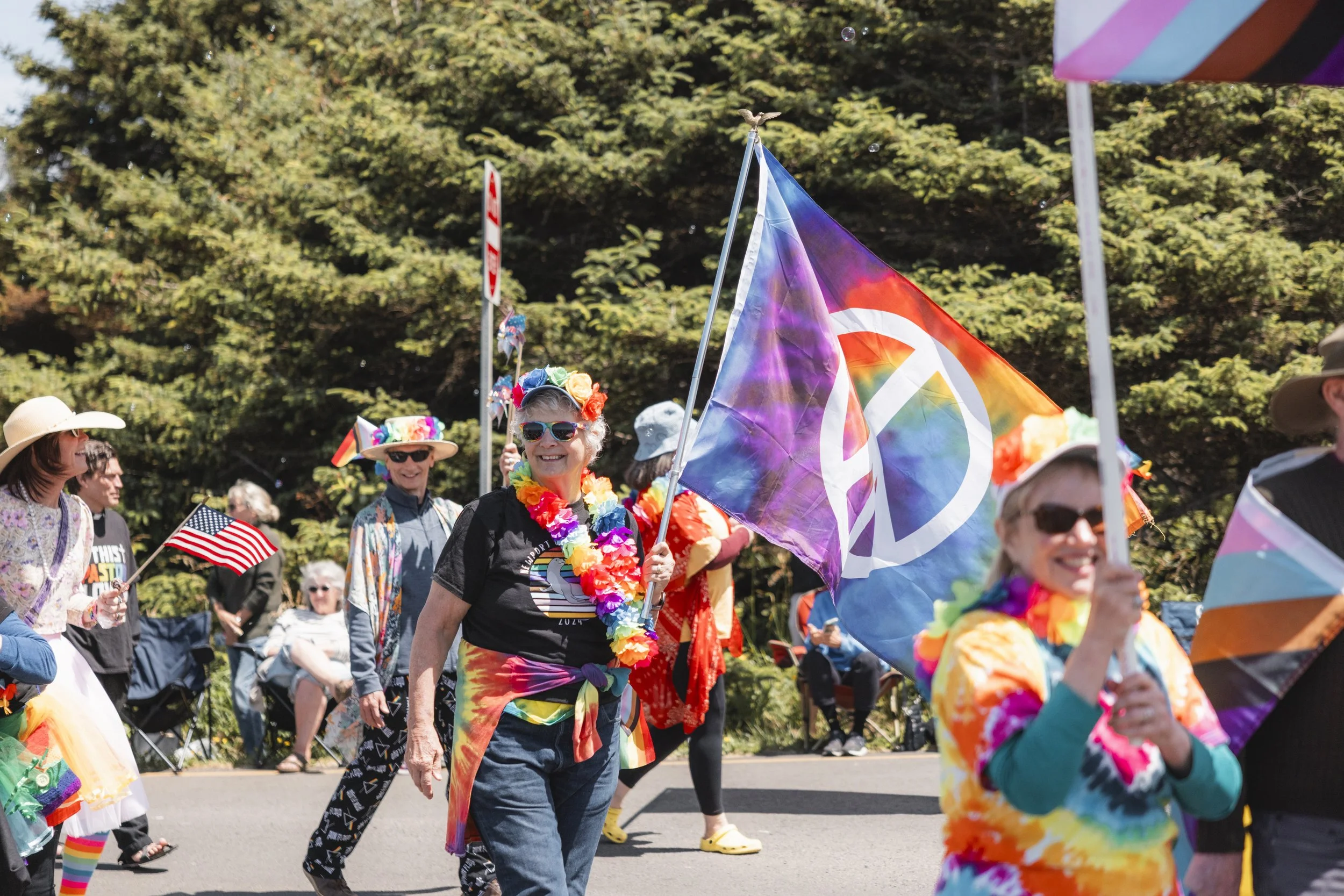 People participating in a Pride parade wearing colorful clothing and accessories, holding rainbow flags and dancing outdoors.