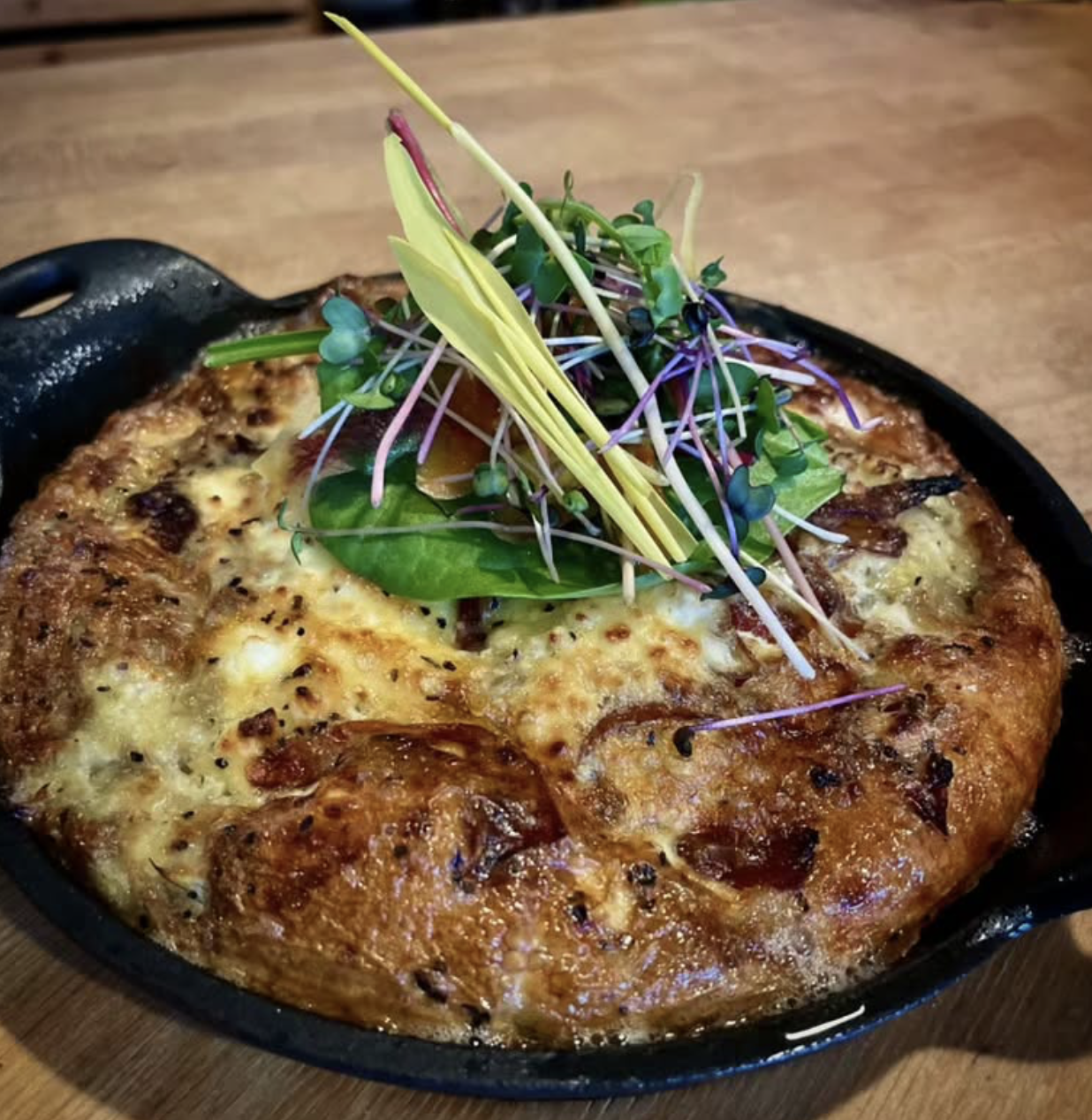 Baked cheesy dish in a cast iron skillet, topped with microgreens and herbs.