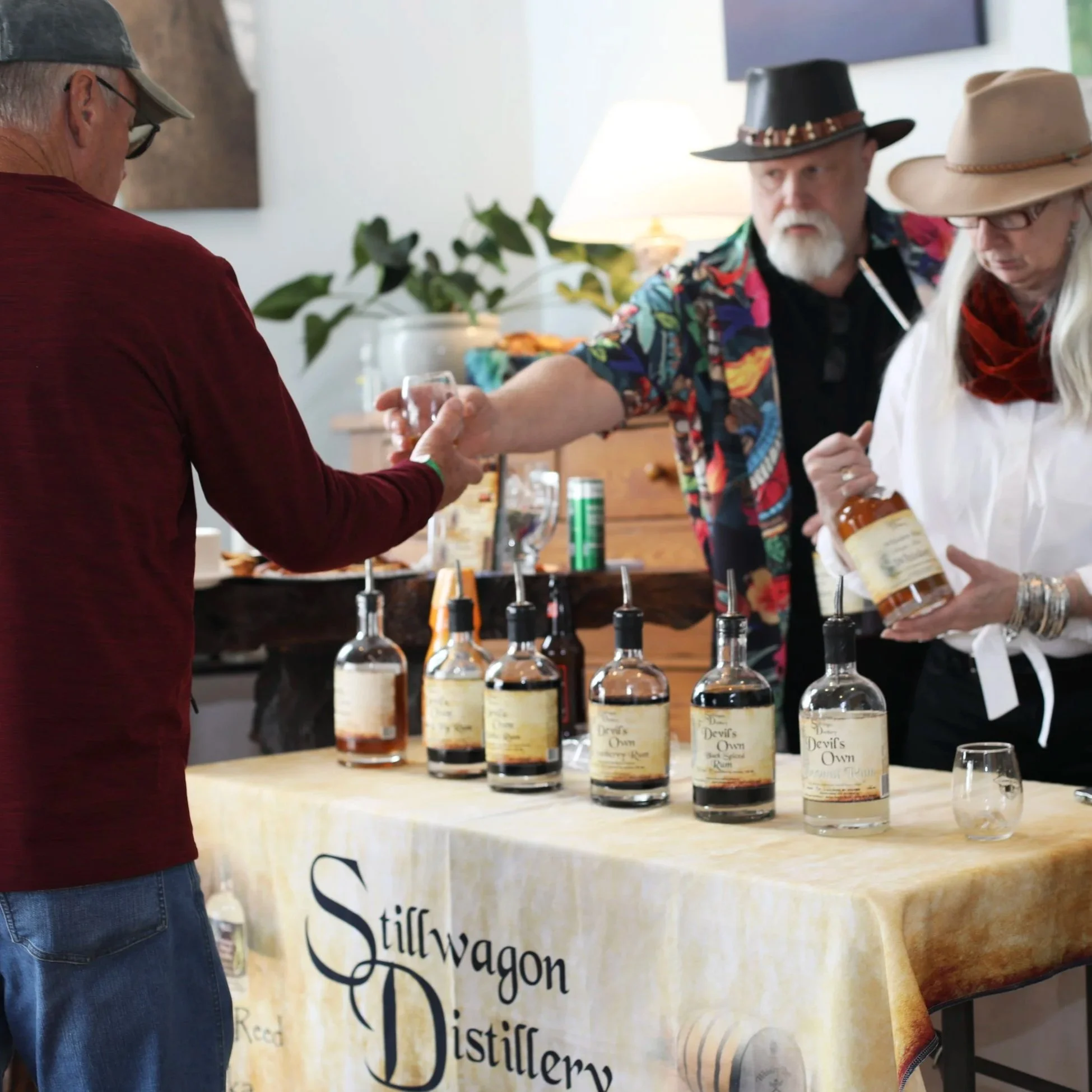 People at Stiffwagon Distillery tasting room booth, with bottles of whiskey on the table, one person pouring a drink for another.