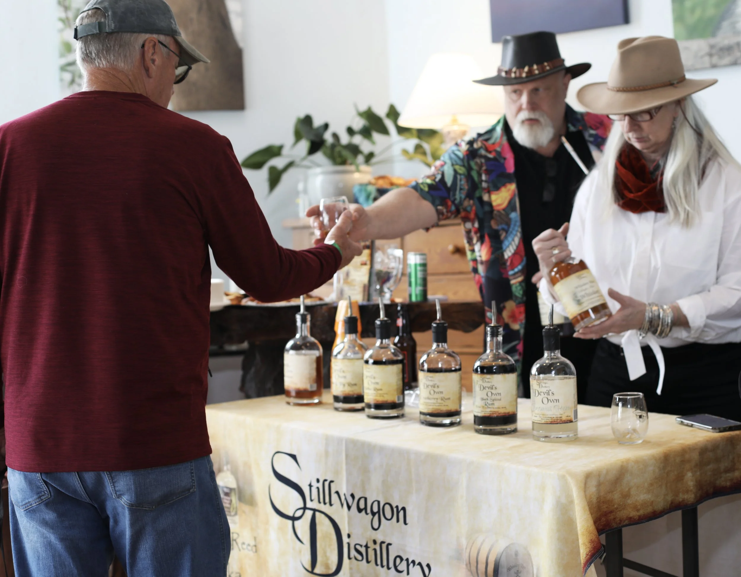 People at a distillery tasting event, with bottles of whiskey on the table.