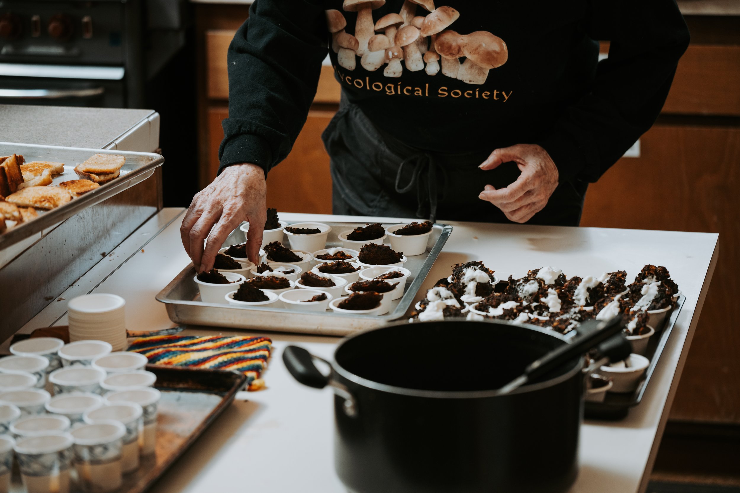 Person preparing chocolate desserts with whipped cream on a kitchen counter, using small bowls and trays.