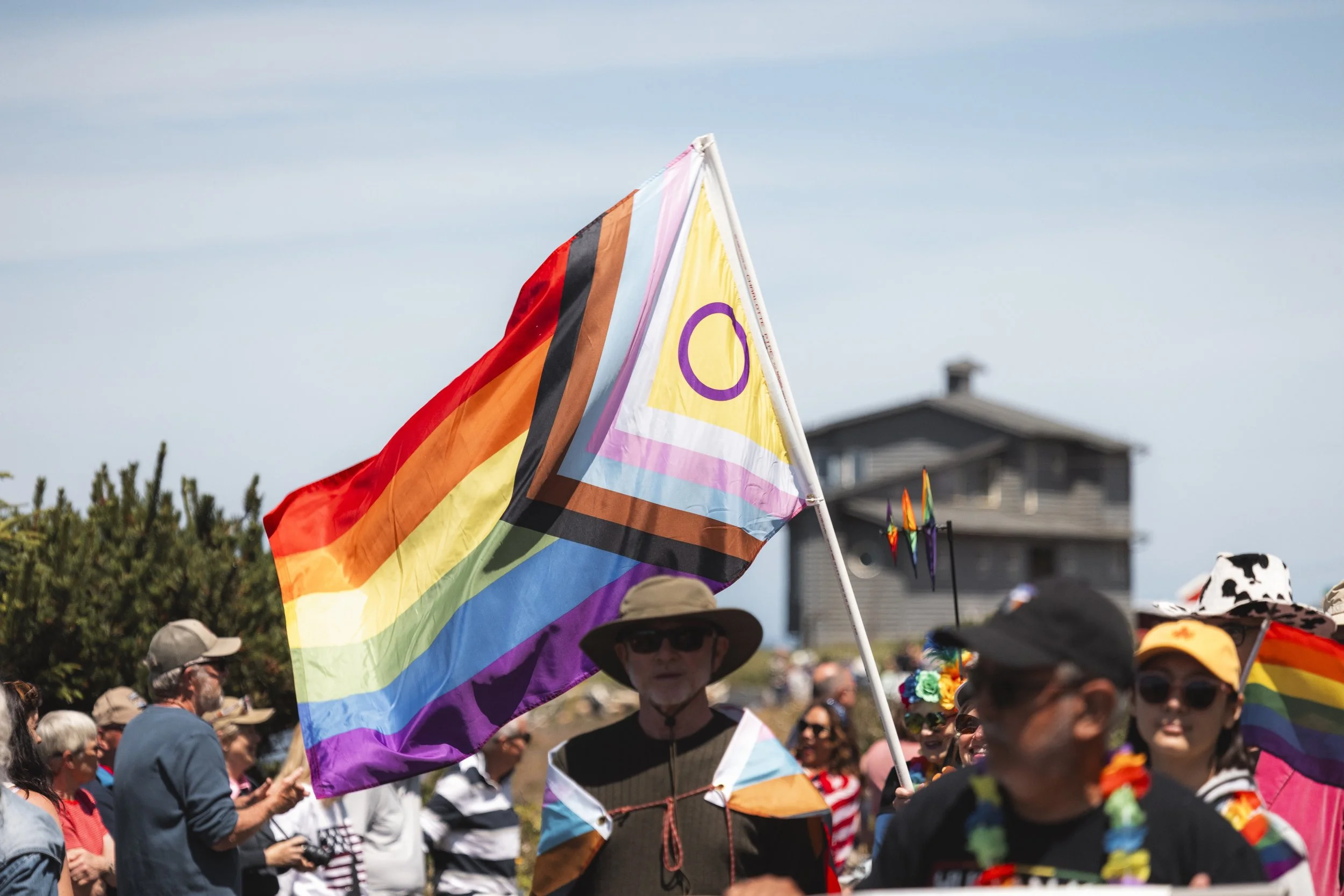 People participating in a pride parade holding rainbow flags and wearing colorful accessories outdoors on a sunny day.