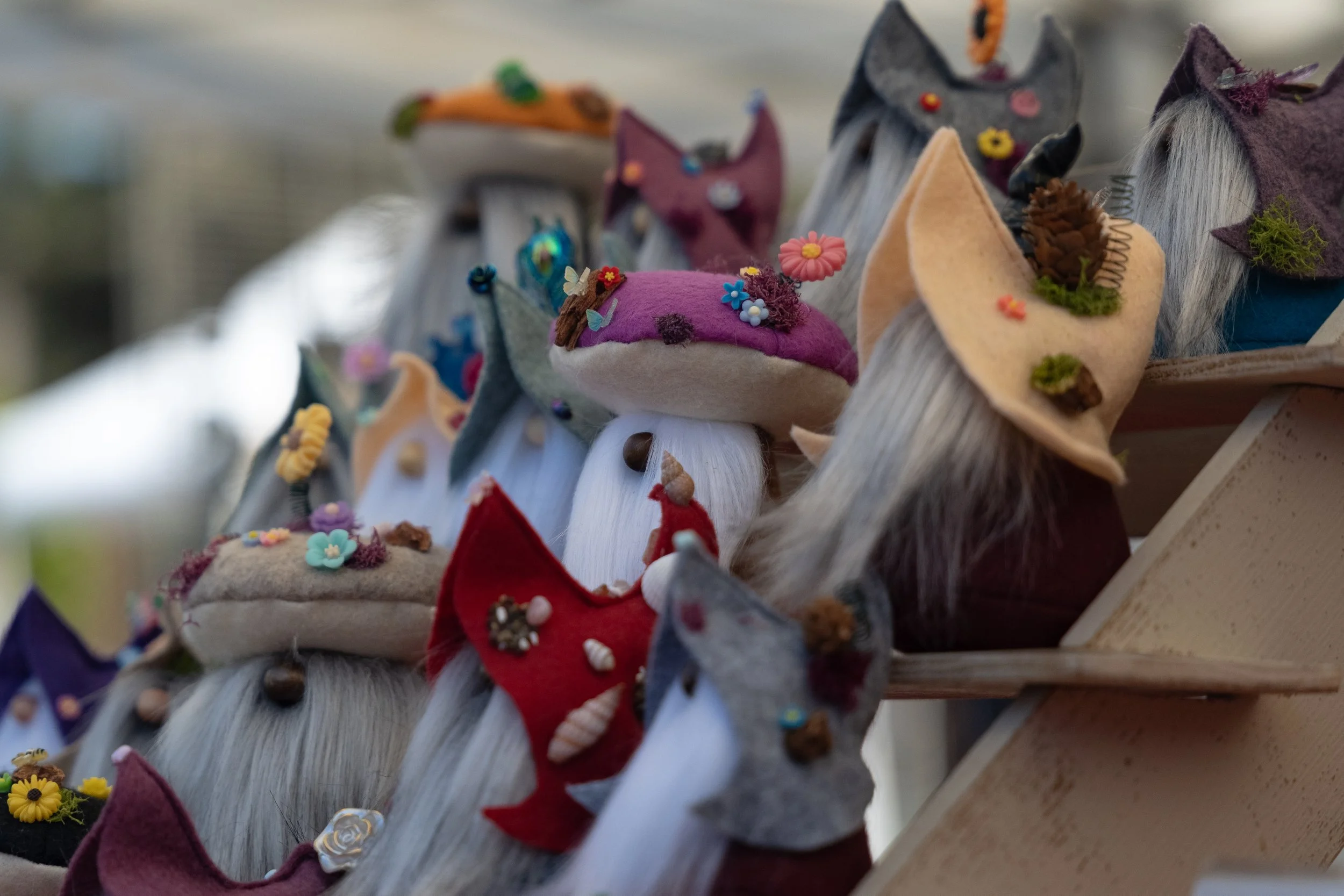 Colorful felt hats decorated with flowers, animals, and small ornaments displayed on a wooden stand.