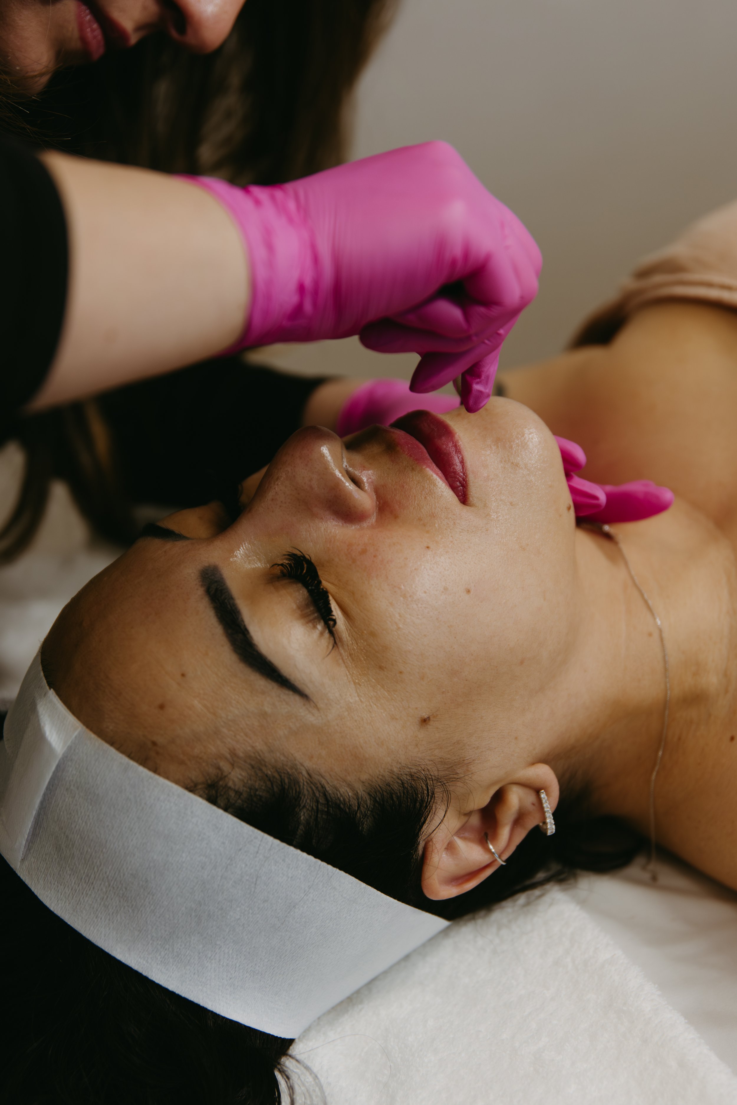 A woman receiving a cosmetic procedure on her lips from a practitioner wearing pink gloves.
