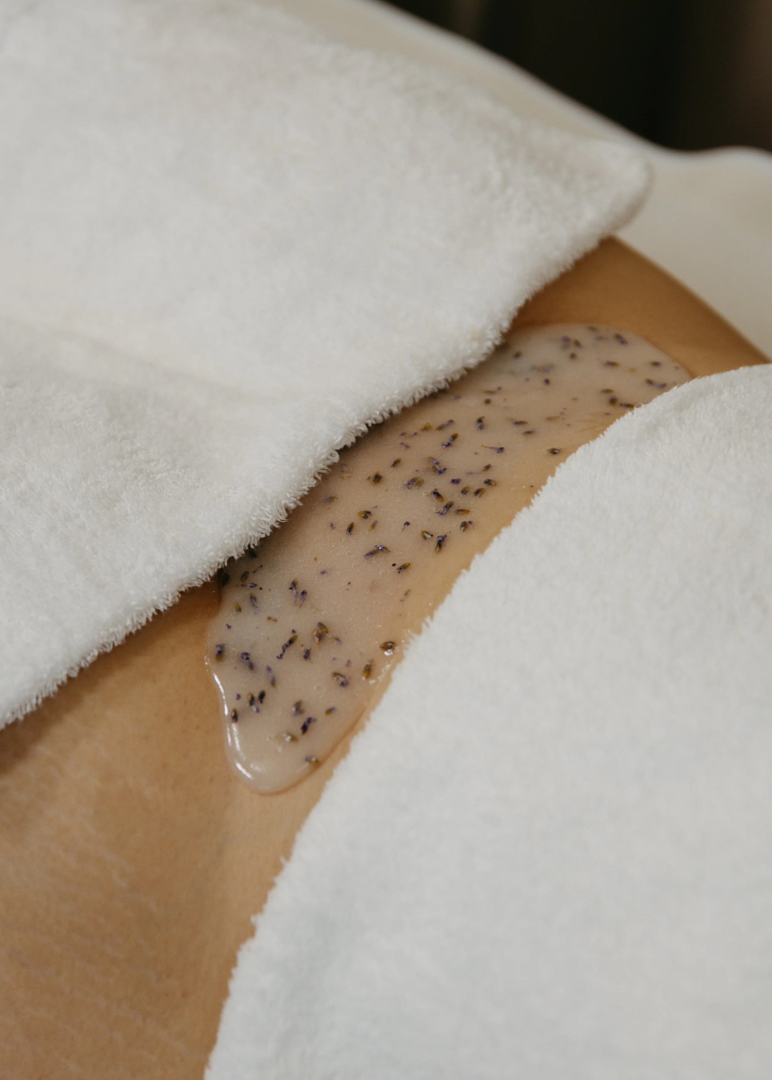 A person receiving a hot stone massage with lavender oil on their back, covered with white towels.