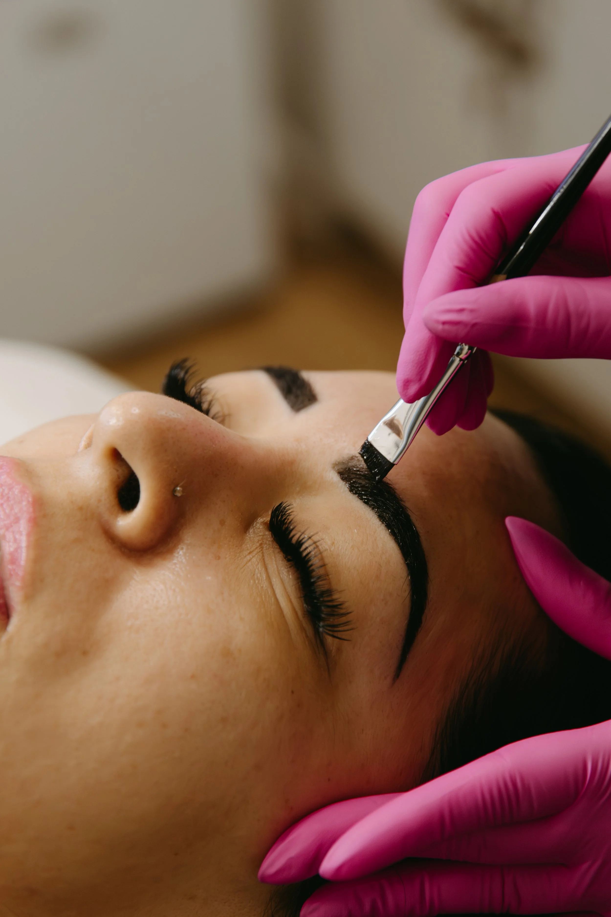 Close-up of a woman getting her eyebrows tattooed or microbladed with a tool, wearing pink gloves.