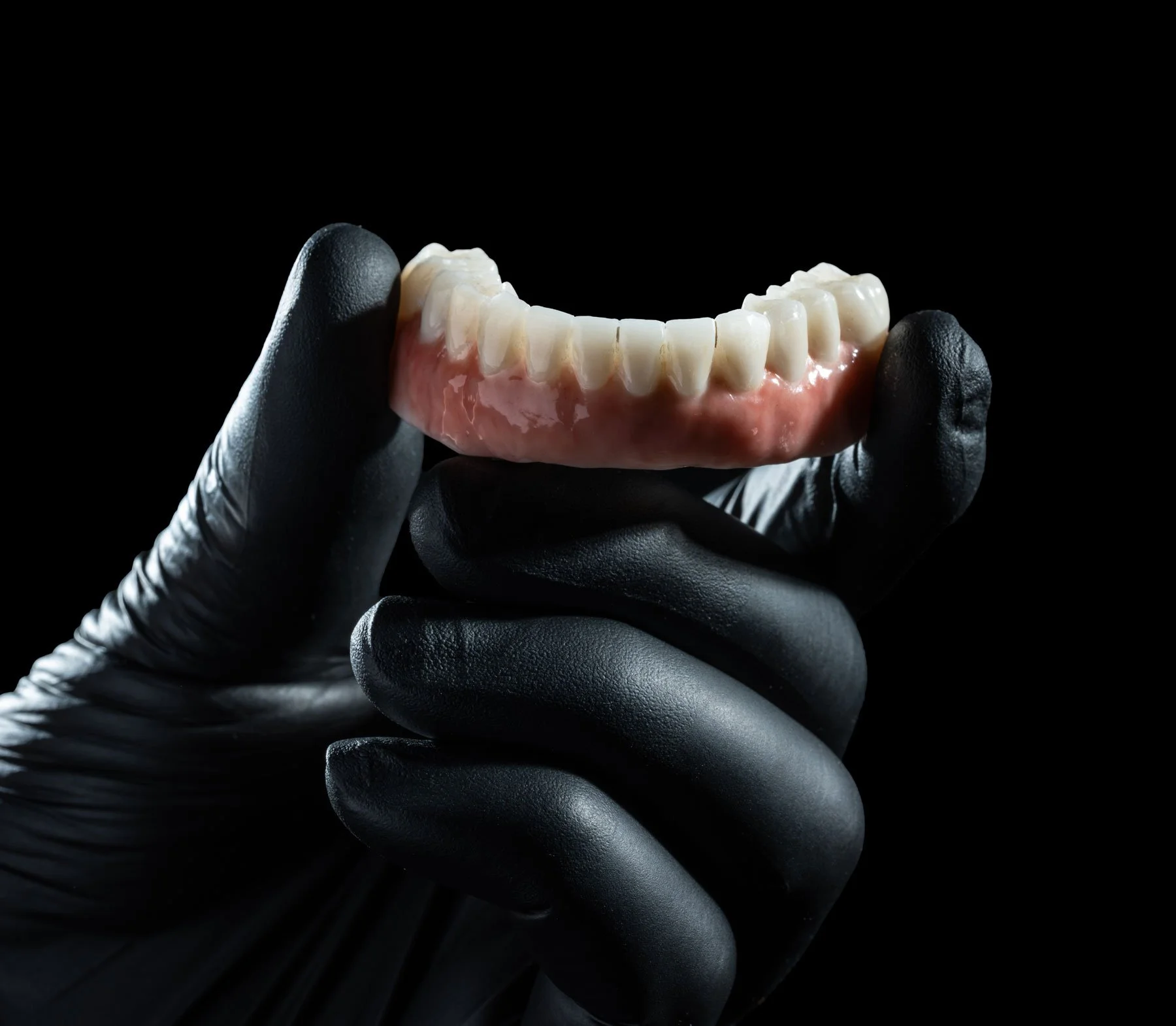 A gloved hand holding a set of false teeth or dentures against a black background.