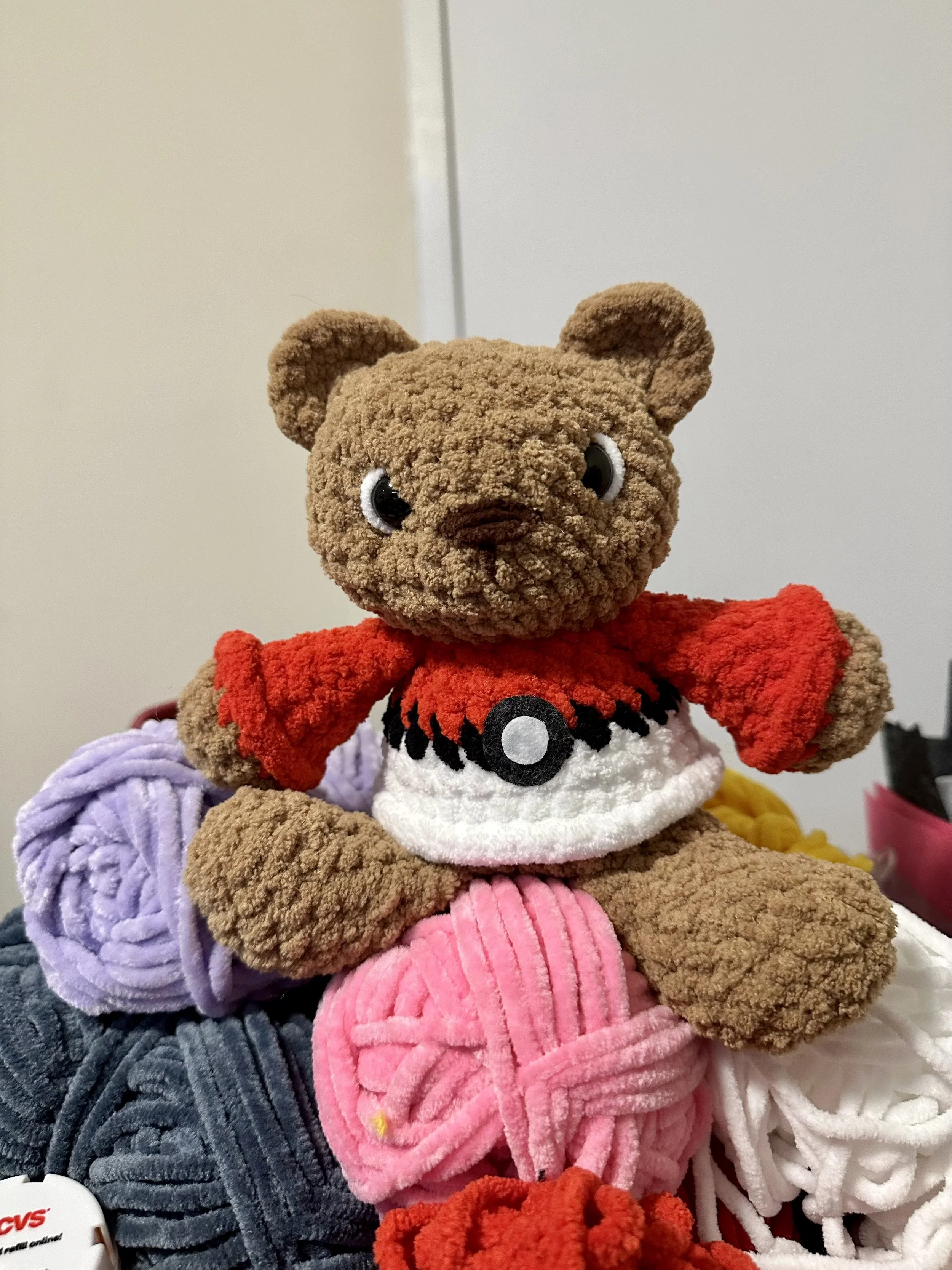 A brown crochet teddy bear with a pokéball sweatshirt