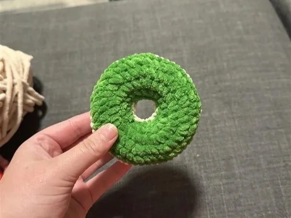 hand holding a crocheted donut with green yarn