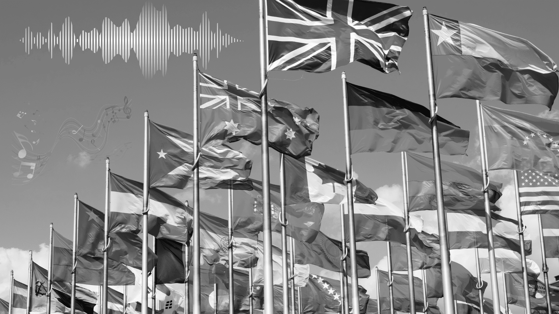 Multiple international flags on flagpoles waving in the wind against a cloudy sky.