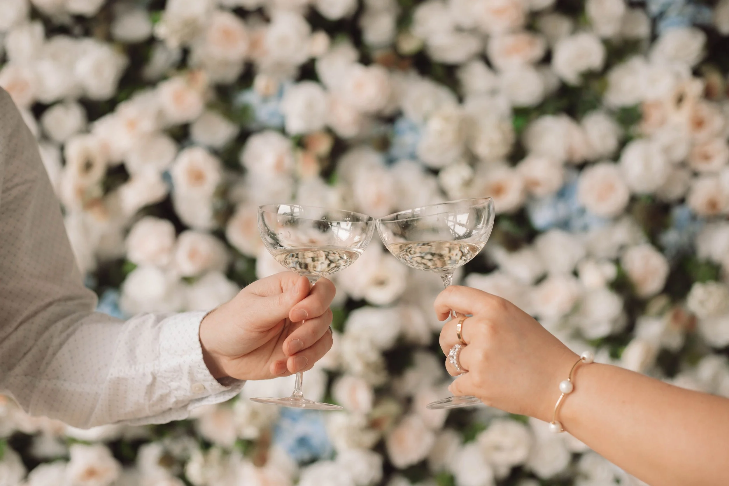 Two people toasting with glasses of champagne against a backdrop of white and pink roses.