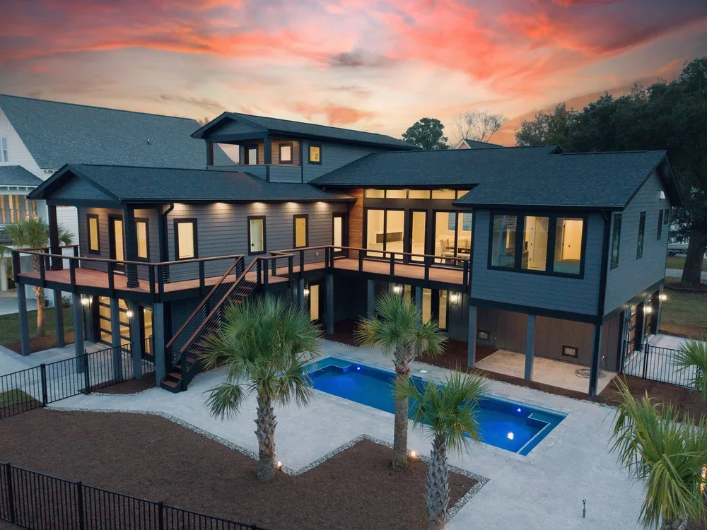 Modern two-story house with a pool and palm trees in backyard at sunset