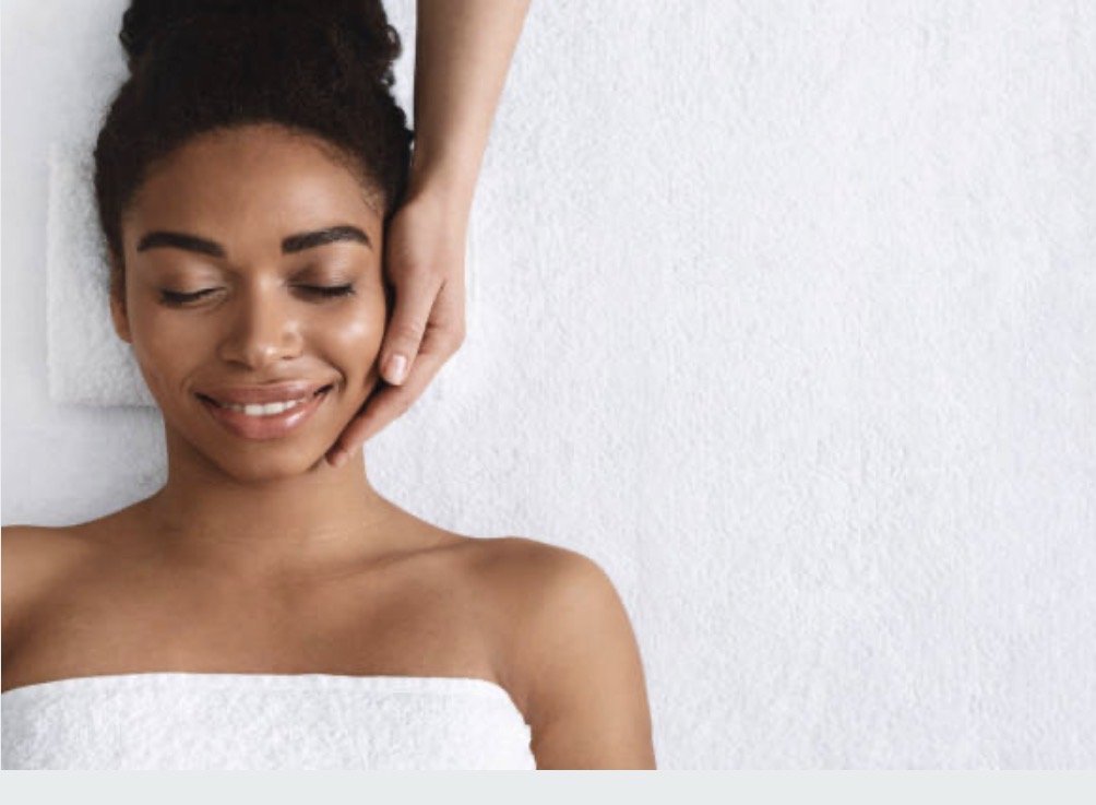 A woman receiving a facial massage, lying down with her eyes closed, in a spa or wellness setting.