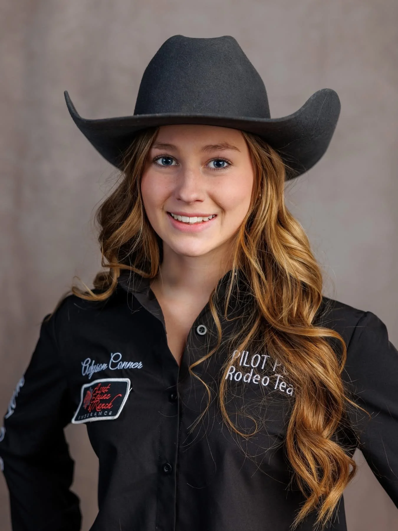 A young woman dressed in a western cowboy outfit, including a large cowboy hat, standing in front of a fountain inside a building, holding cash and jewelry and smiling.