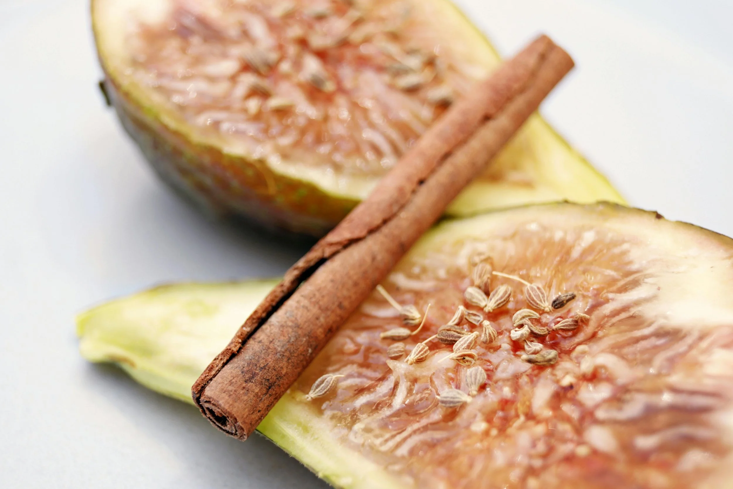 Close-up of a halved fig with seeds and a cinnamon stick on top of a slice of fig on a white background.