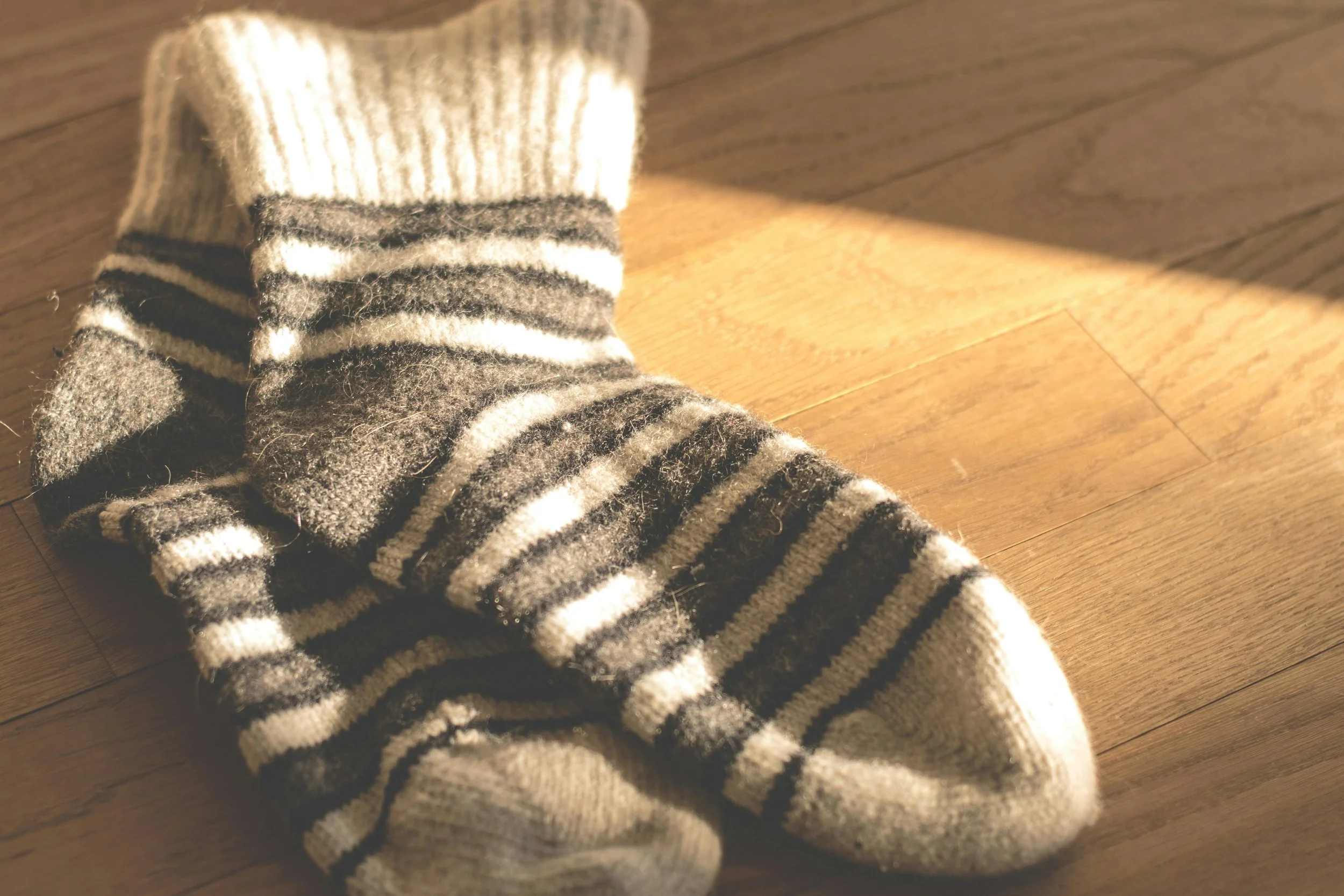 A pair of striped wool socks lying on a wooden floor, illuminated by warm sunlight.