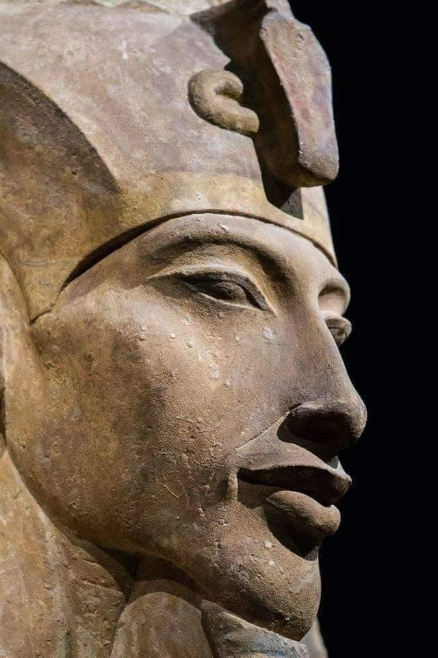 Detailaufnahme einer antiken ägyptischen Skulptur eines Pharao-Gesichts, mit Kopfschmuck und hieroglyphischem Dekor.