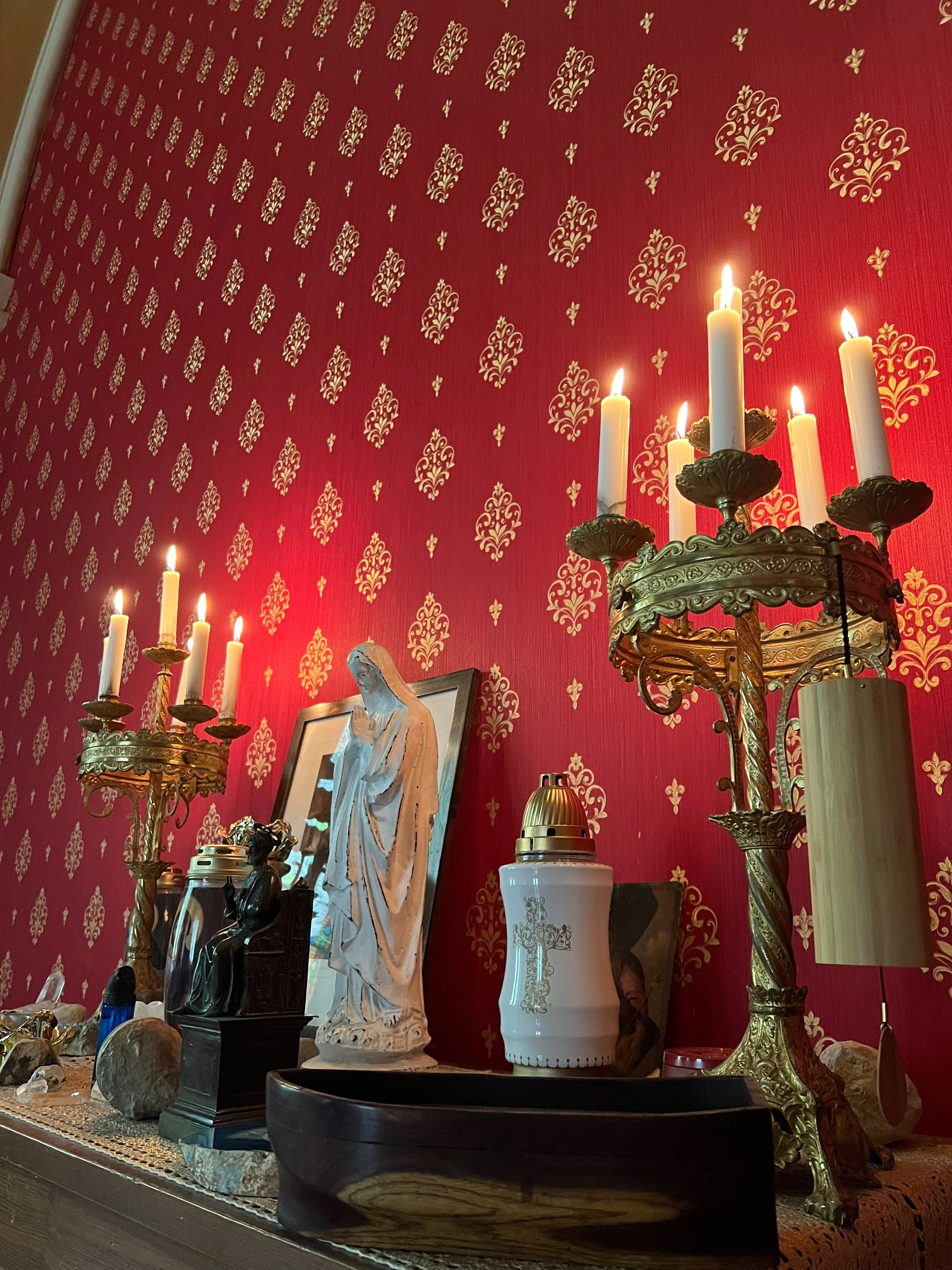 Ein Altar mit Kerzenleuchtern, Statuen und religiösen Gegenständen vor einer roten Wand mit goldenen Mustern.