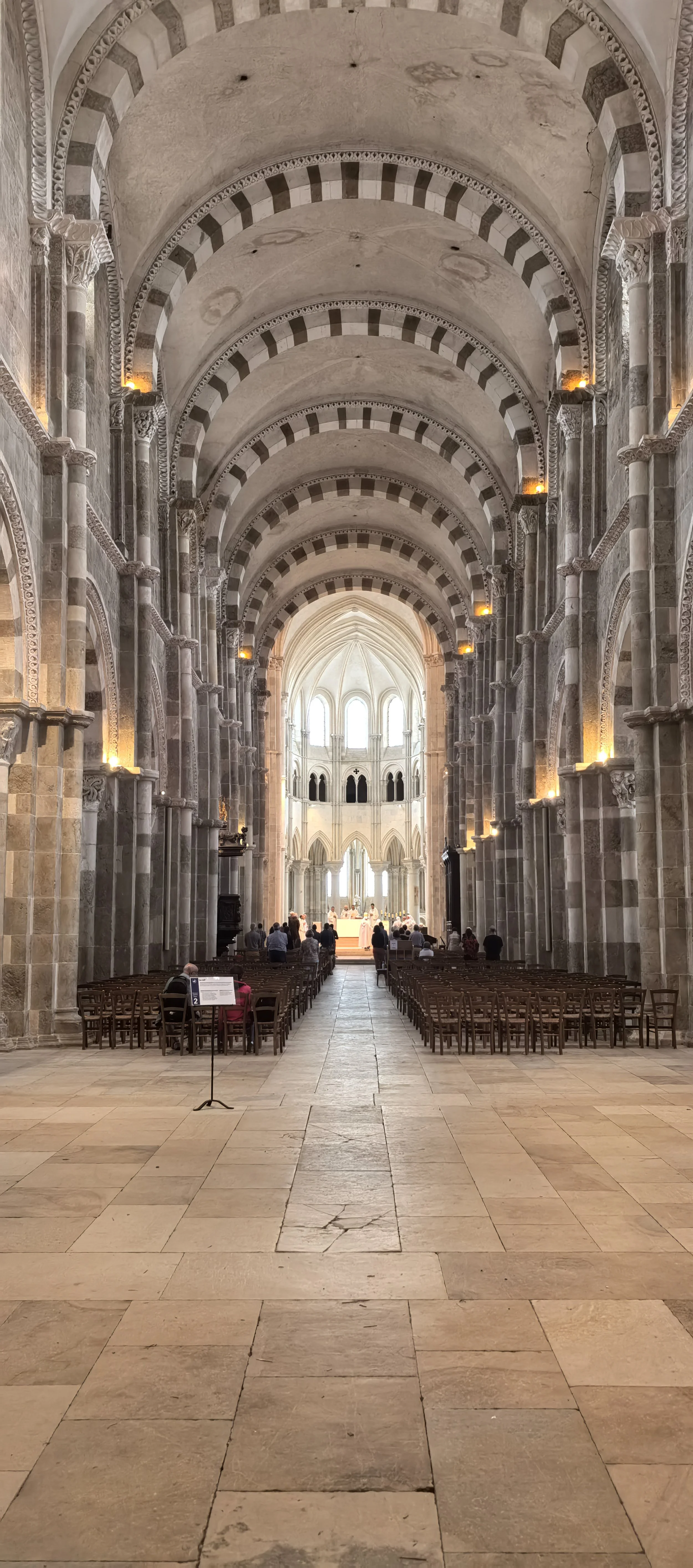 Innenansicht einer großen gotischen Kirche mit hohen Gewölbedecken, steinernen Säulen und Bänken, Menschen beim Gebet.
