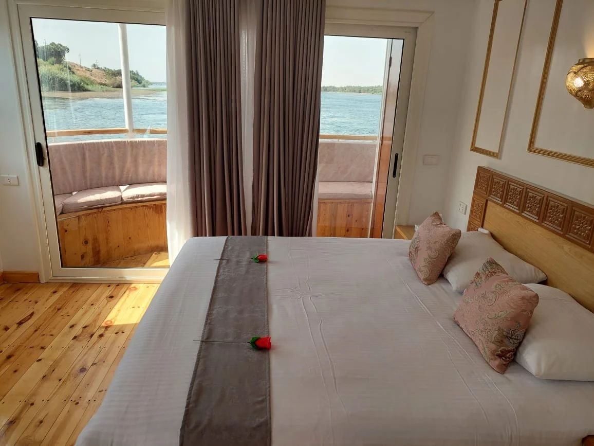 Hotelzimmer mit Bett, zwei Kissen, Blick auf den Fluss über Balkon und Fenster, Dekoration an der Wand, Holzfußboden.