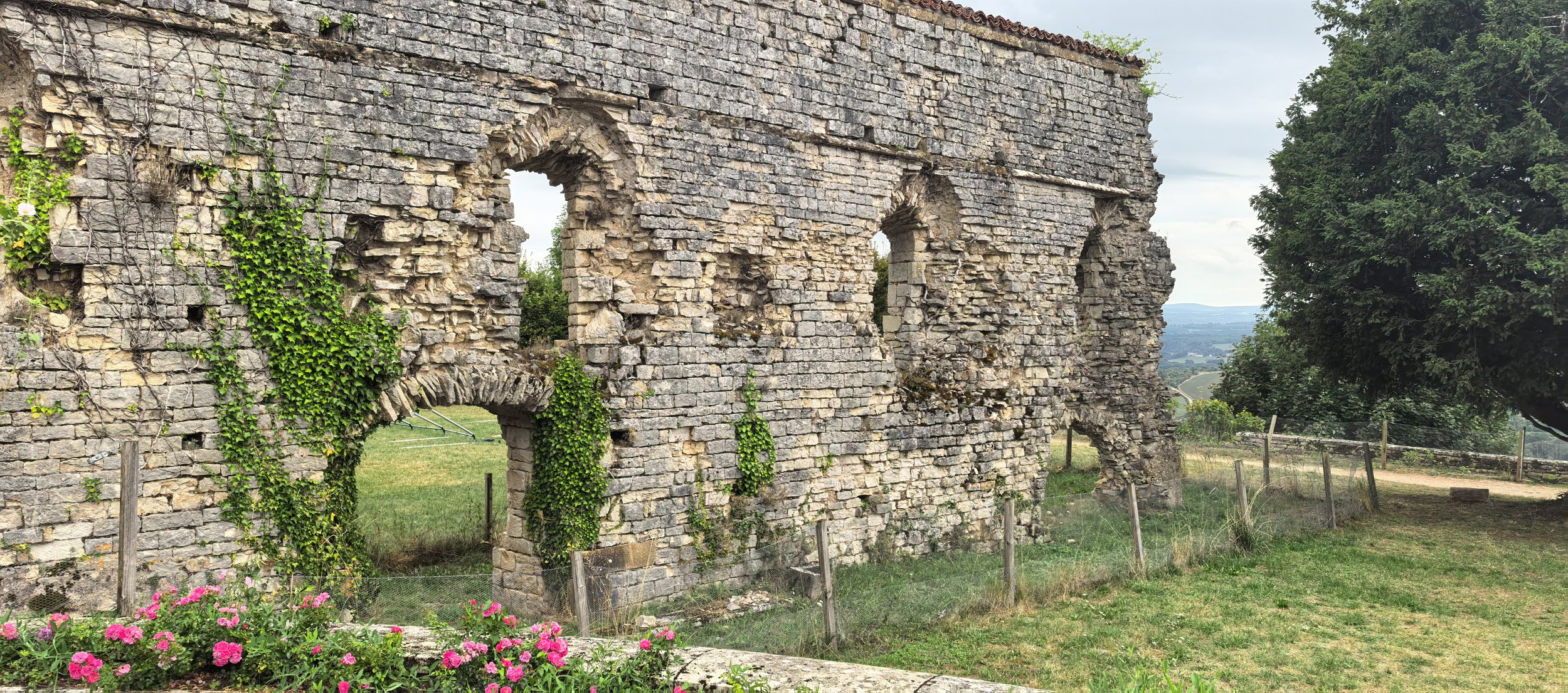 Verfallene Steinvilla im Grünen mit Bäumen und Feldern im Hintergrund.