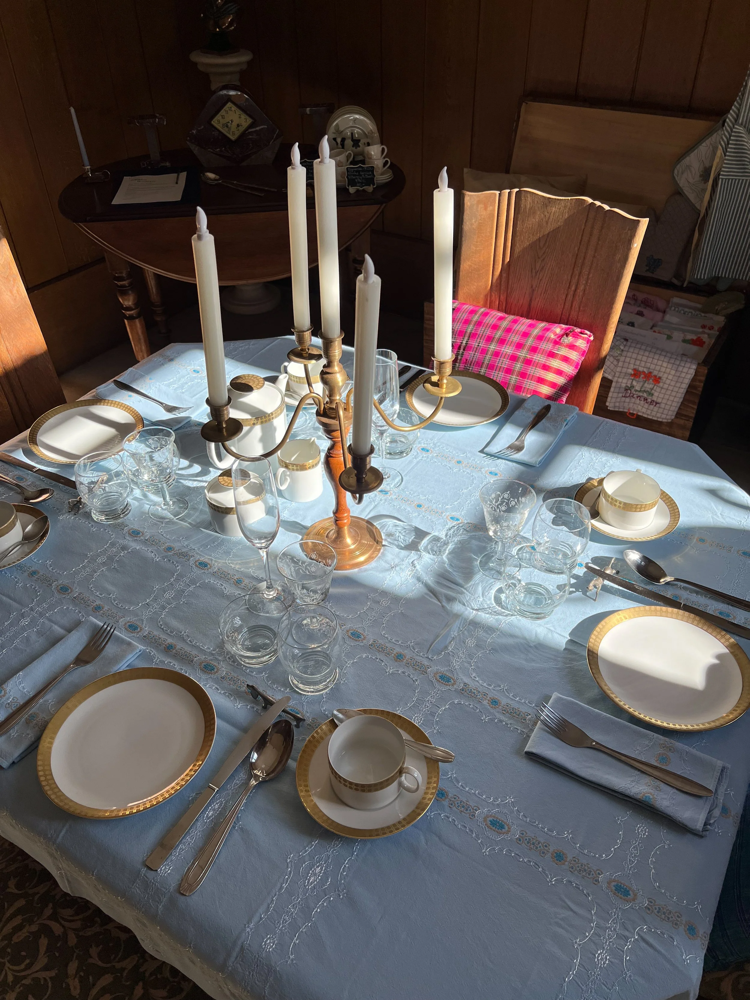 Ein schön gedeckter Esstisch mit weißen Geschirr, Gläsern, Messer, Gabeln, Löffeln und einer Kerzenleuchter mit weißen Kerzen. Der Tisch ist mit einer weißen Tischdecke bedeckt.